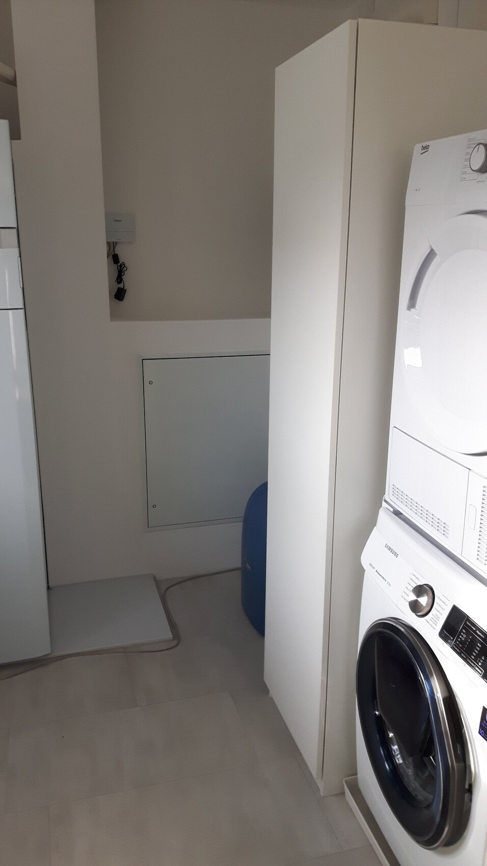 Washing machine on the bottom, dryer above, white cabinets, blue water tank in the background.