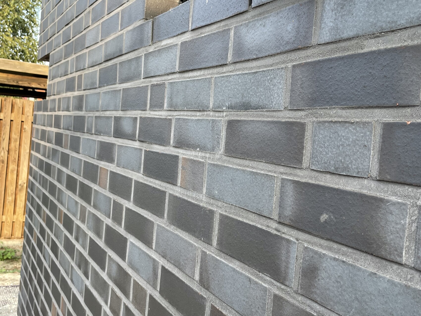 Dark gray brick wall, wooden slat fence visible on the side.