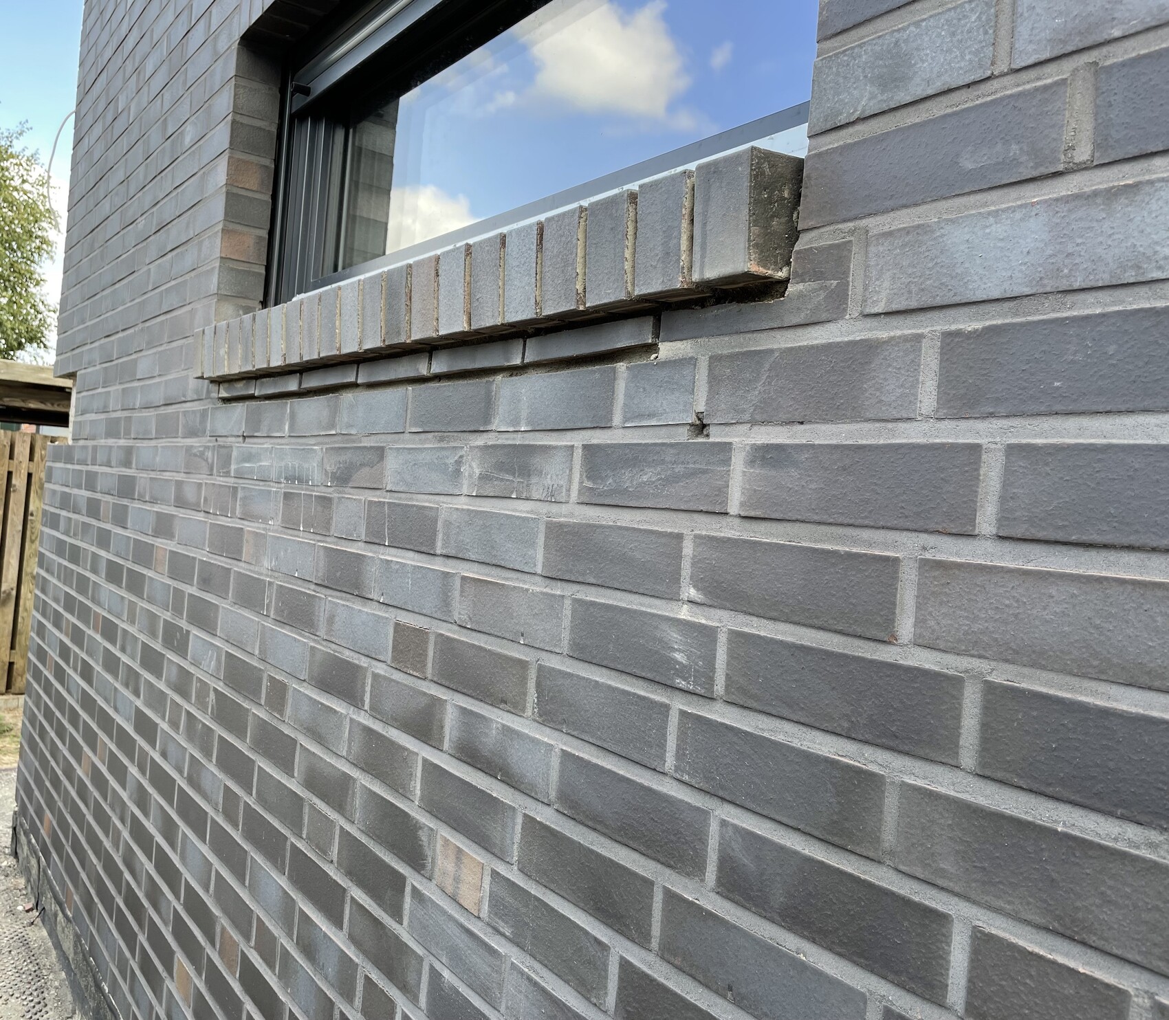 Gray brick façade with narrow window; damaged row of bricks below the window.