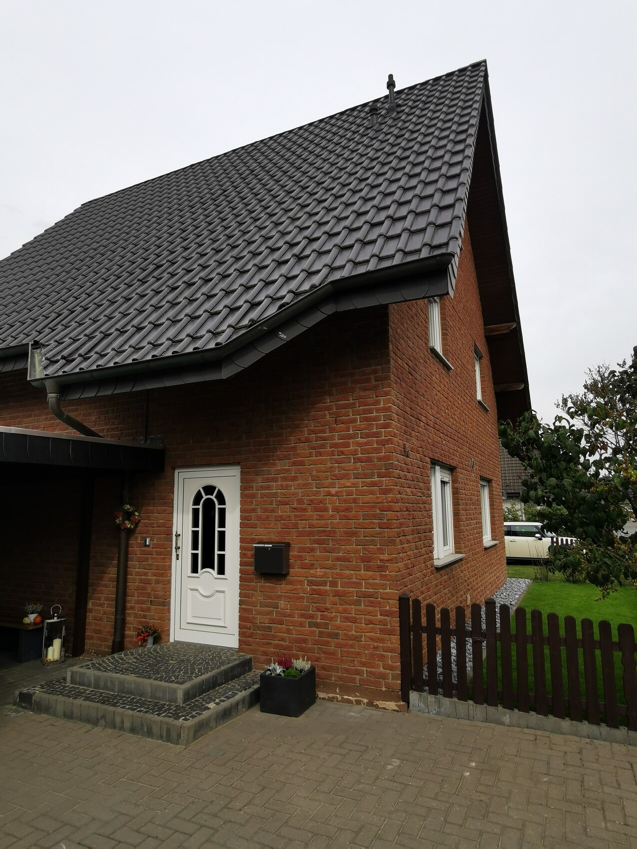 Ziegelhaus mit steilem, dunklem Dach, weißer Tür und kleinem Vorgarten.