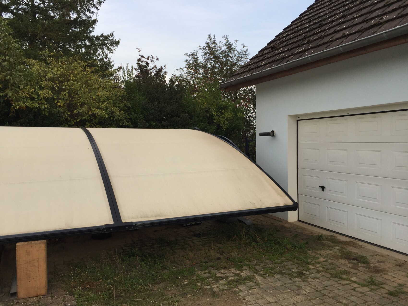 Large white, curved pool cover in front of a house garage.