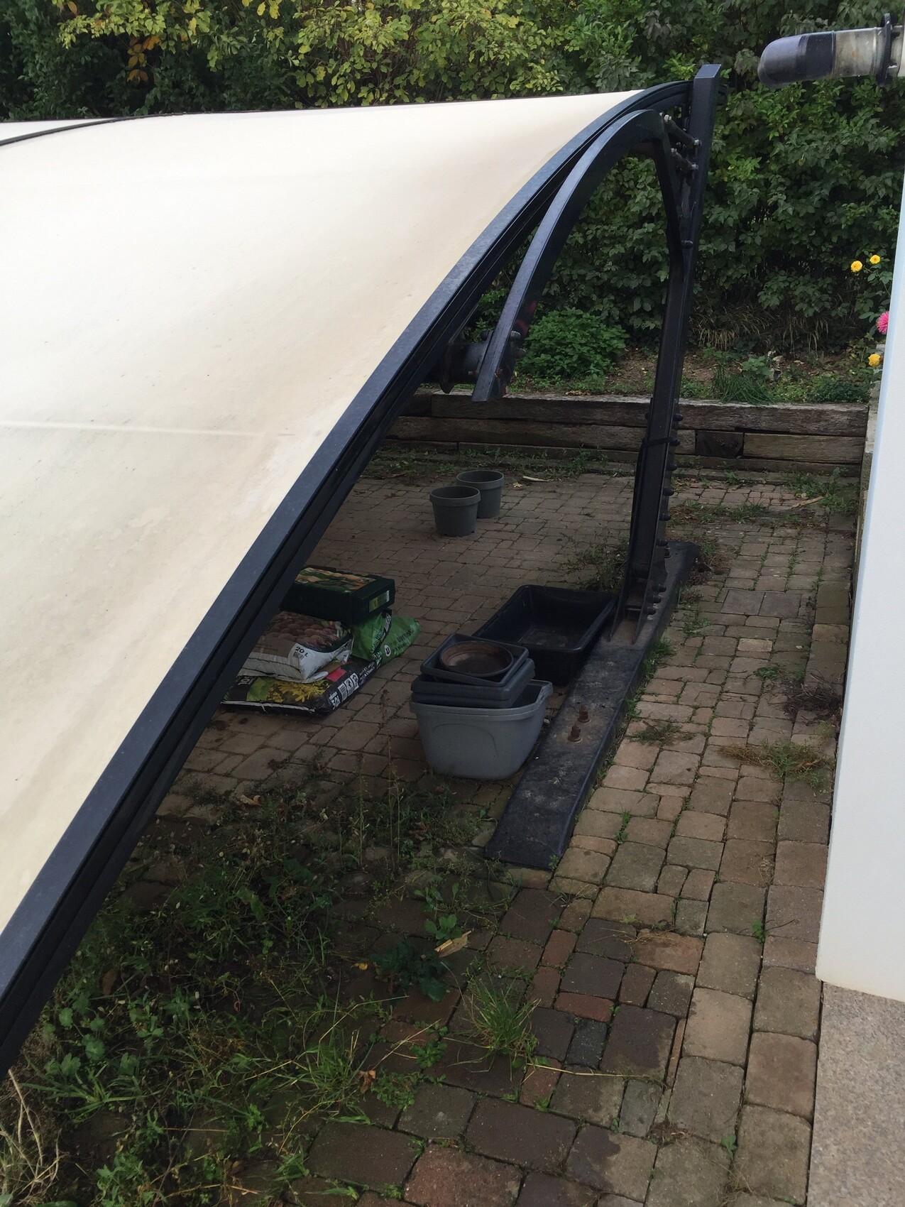White tarp on black metal frame in the garden, next to gray storage boxes.