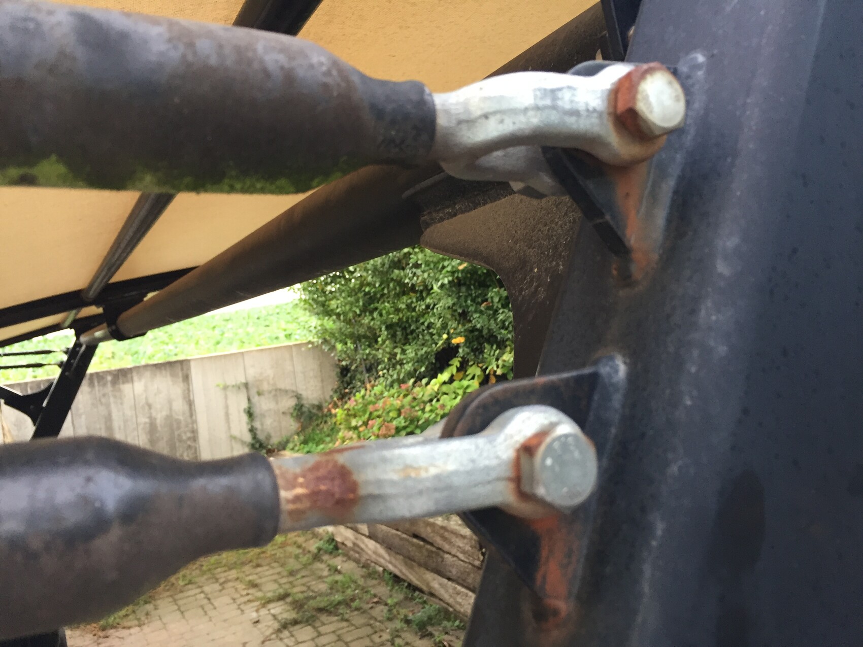 Close-up of a rusty bolt on a metal arm of the frame; garden in the background.