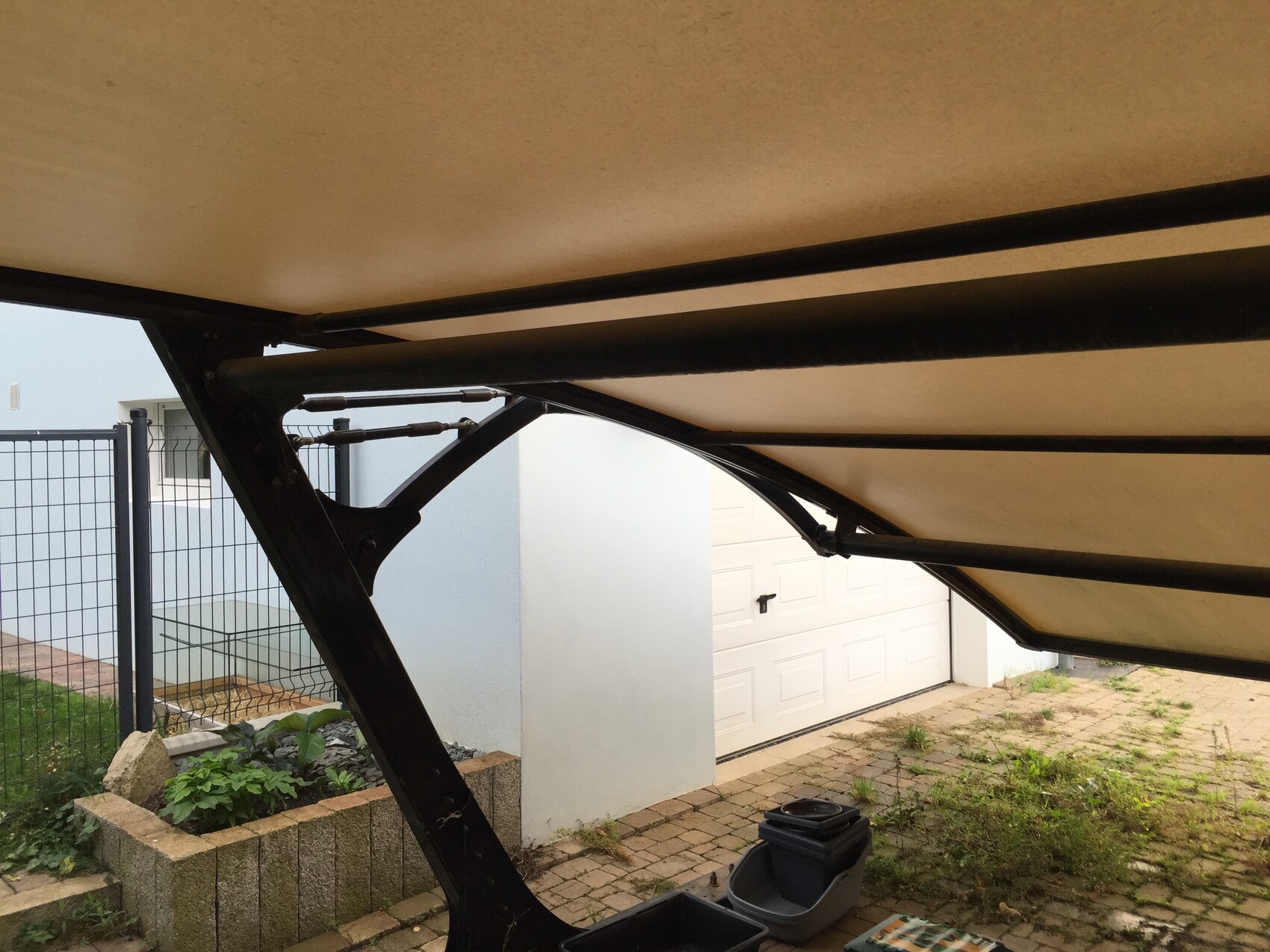 Underside of a folding patio roof with beige fabric and black metal frame.