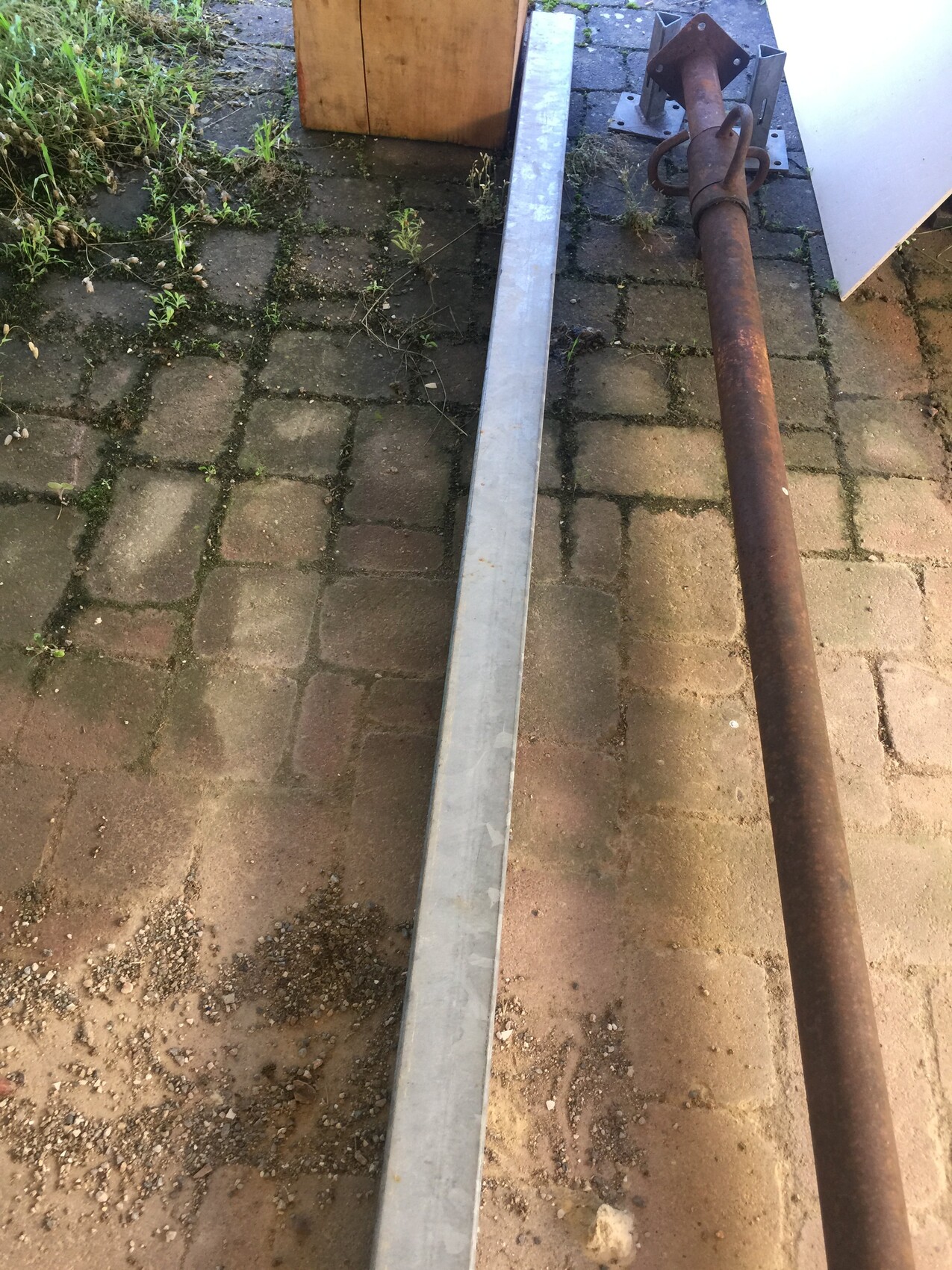 Rusty pipe with flange lying next to silver metal profile on paved ground.