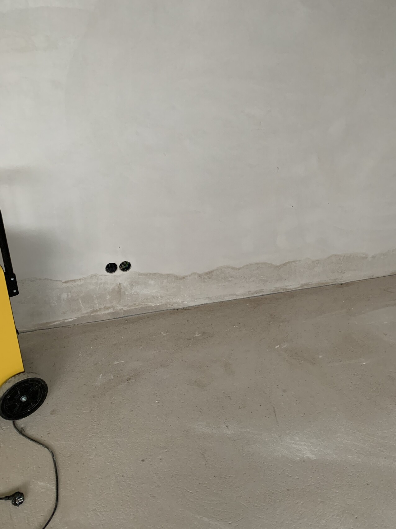 Two round wall openings near the floor, yellow machine with wheels and cables on the floor.