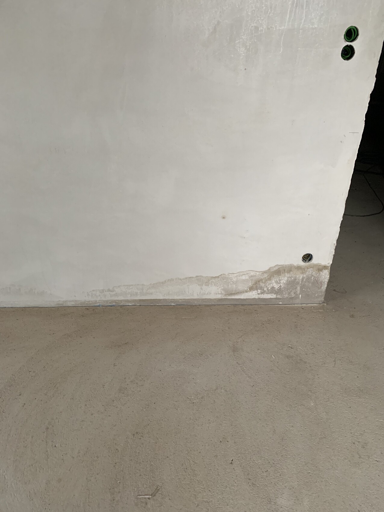White wall with moisture damage and peeling plaster at the bottom edge, green openings.