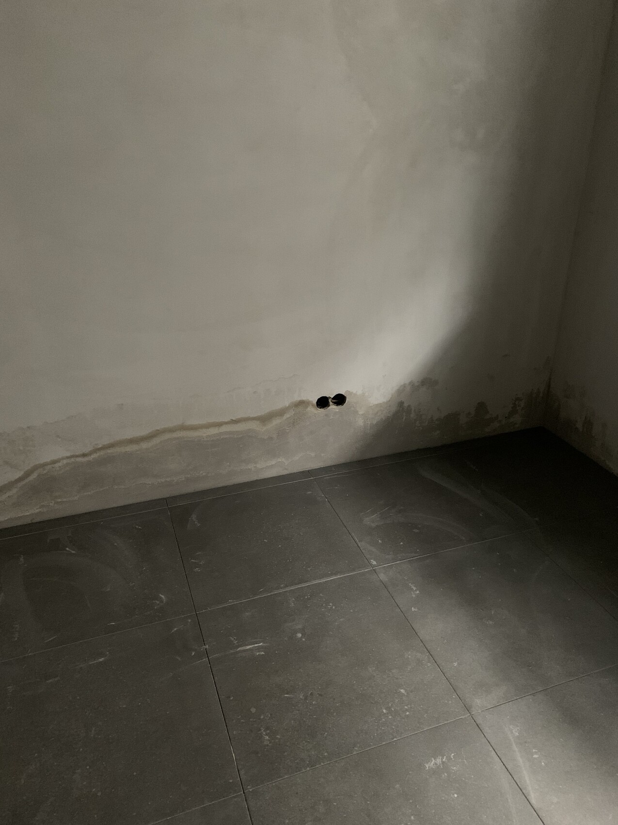 Wall corner with moisture marks, two round holes, dark floor tiles.
