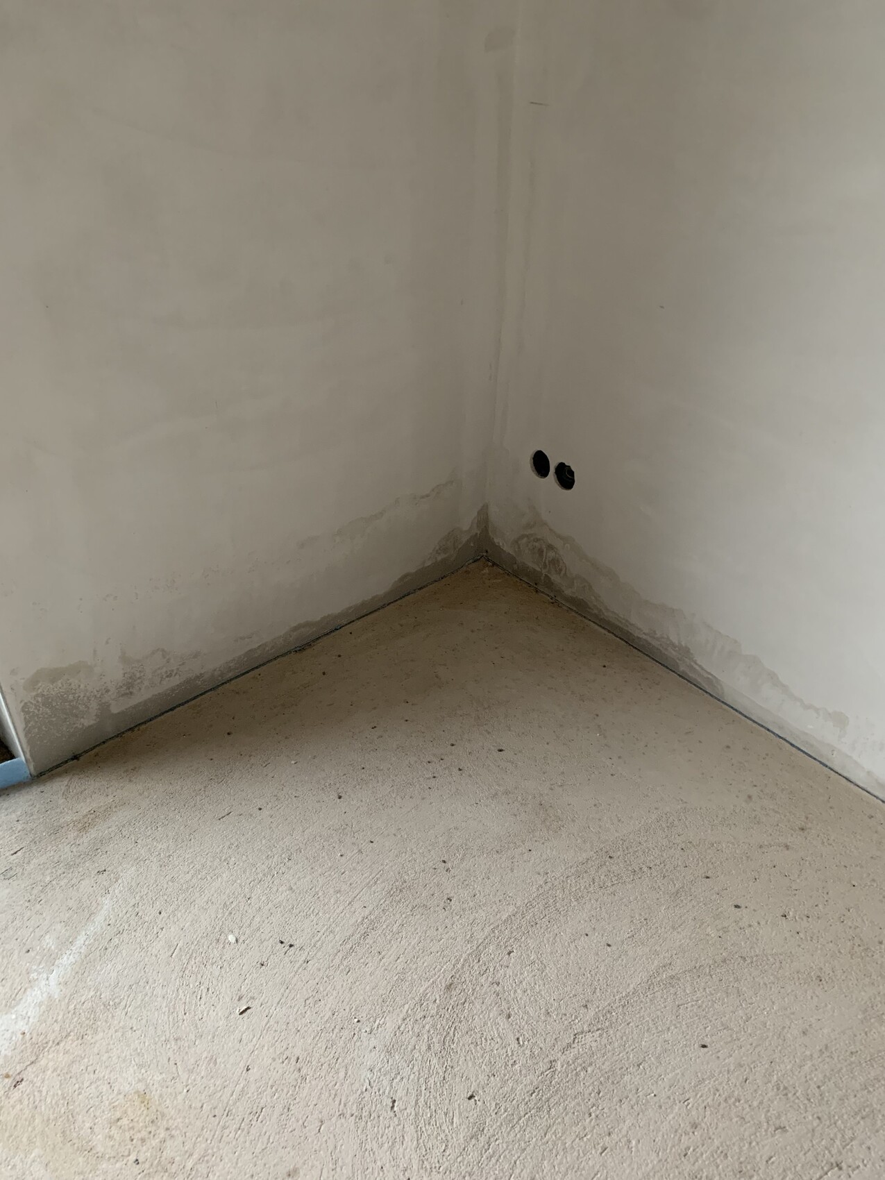 Corner of an unfinished room: white walls, moisture at the bottom, two round wall openings.
