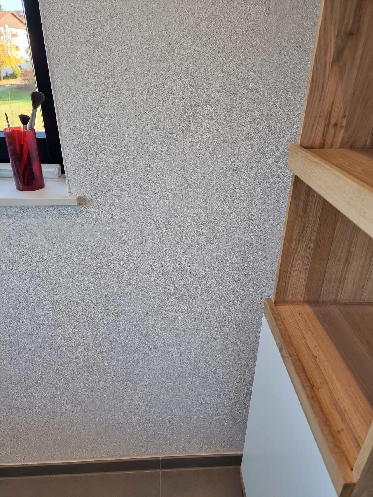 Interior with rough wall texture, window on the left and open wooden shelf on the right.