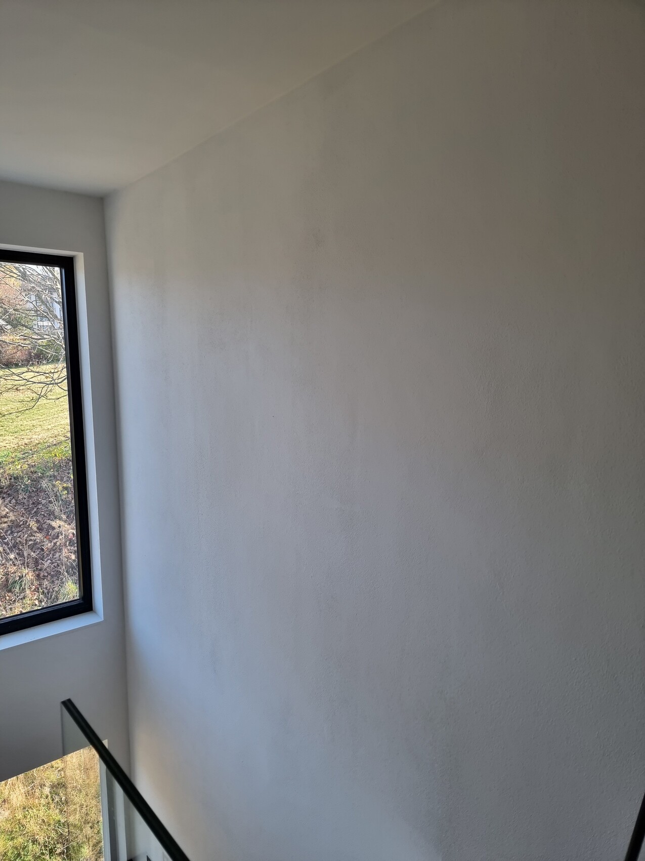 White interior wall next to a window with a view outside to grass and trees.