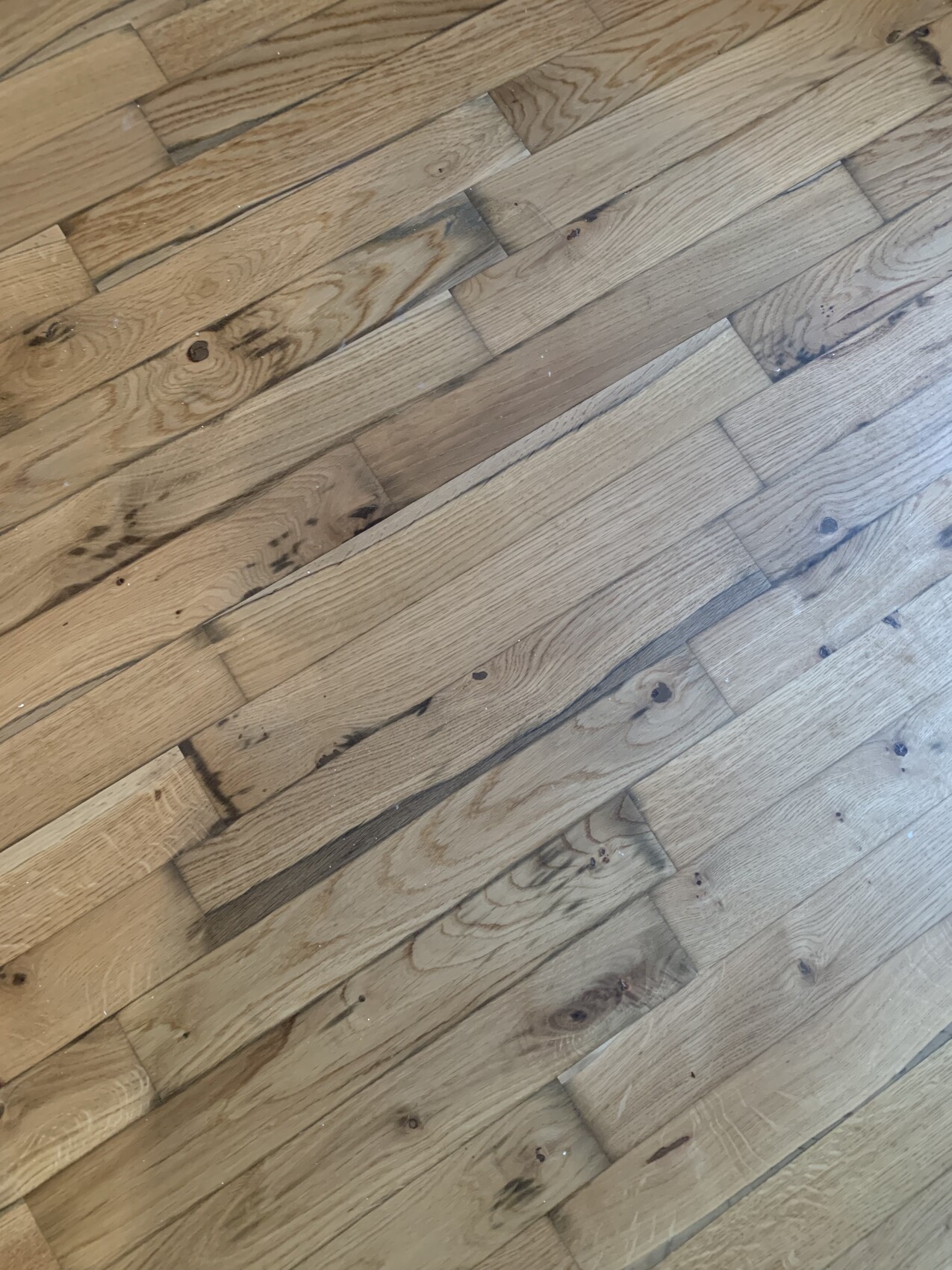 Wood floor with light brown planks, visible grain, some dark spots.