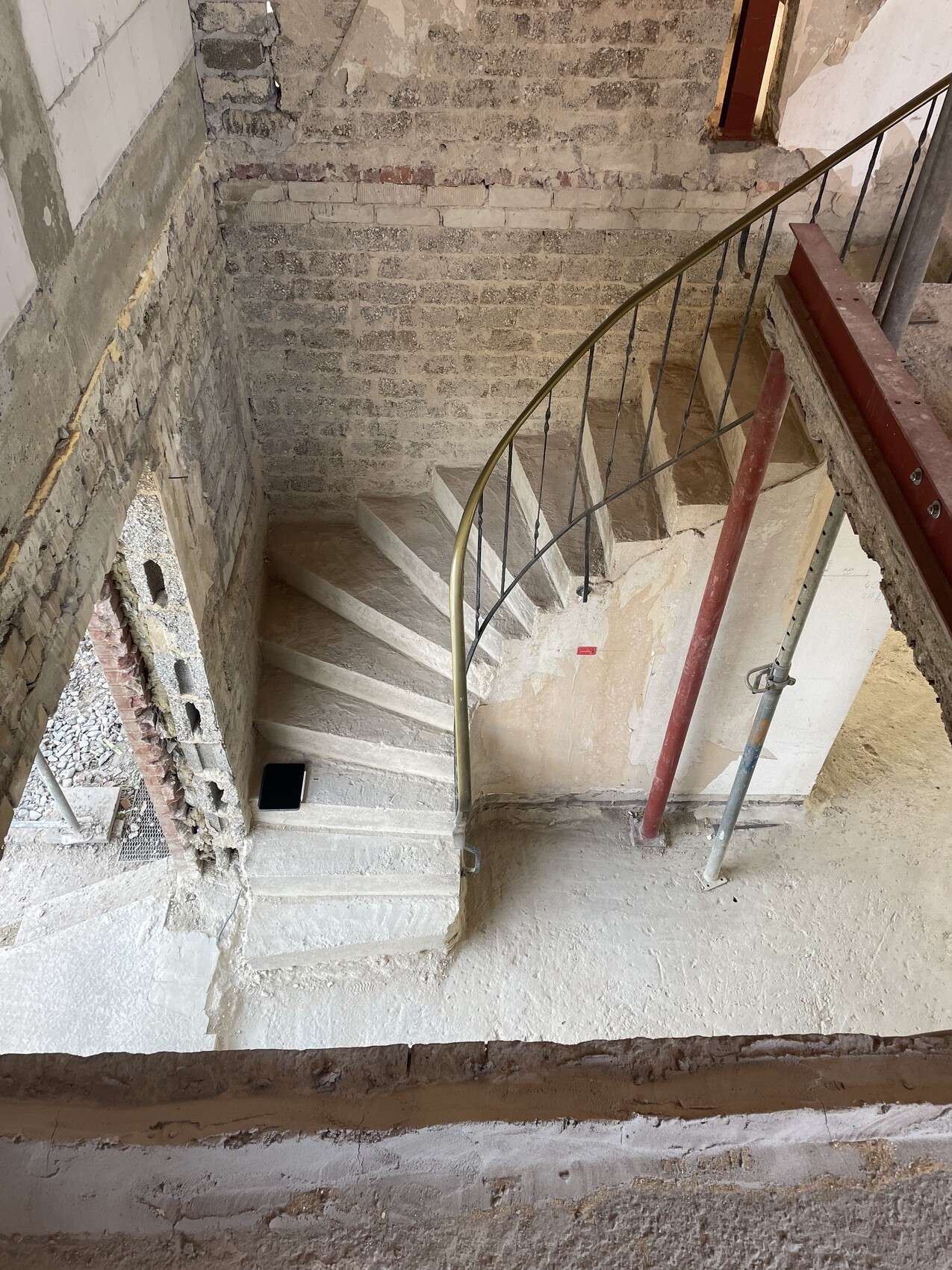 Kurvige Betontreppe auf Baustelle mit Metallhandlauf, roten Stützen und Tablet auf Stufe.