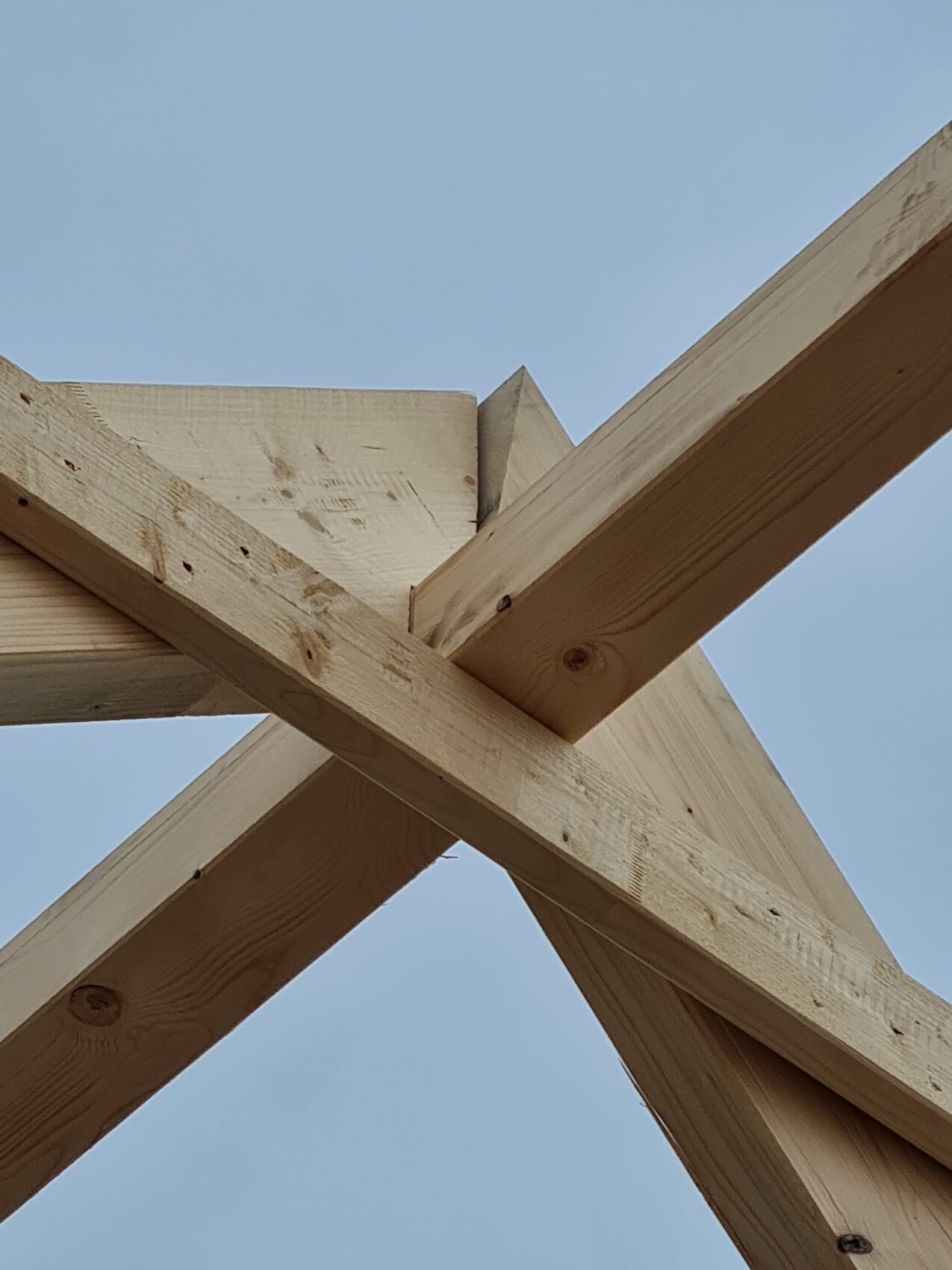Holz-Dachstuhl-Balken kreuzweise verbunden vor blauem Himmel; Aufnahme von unten