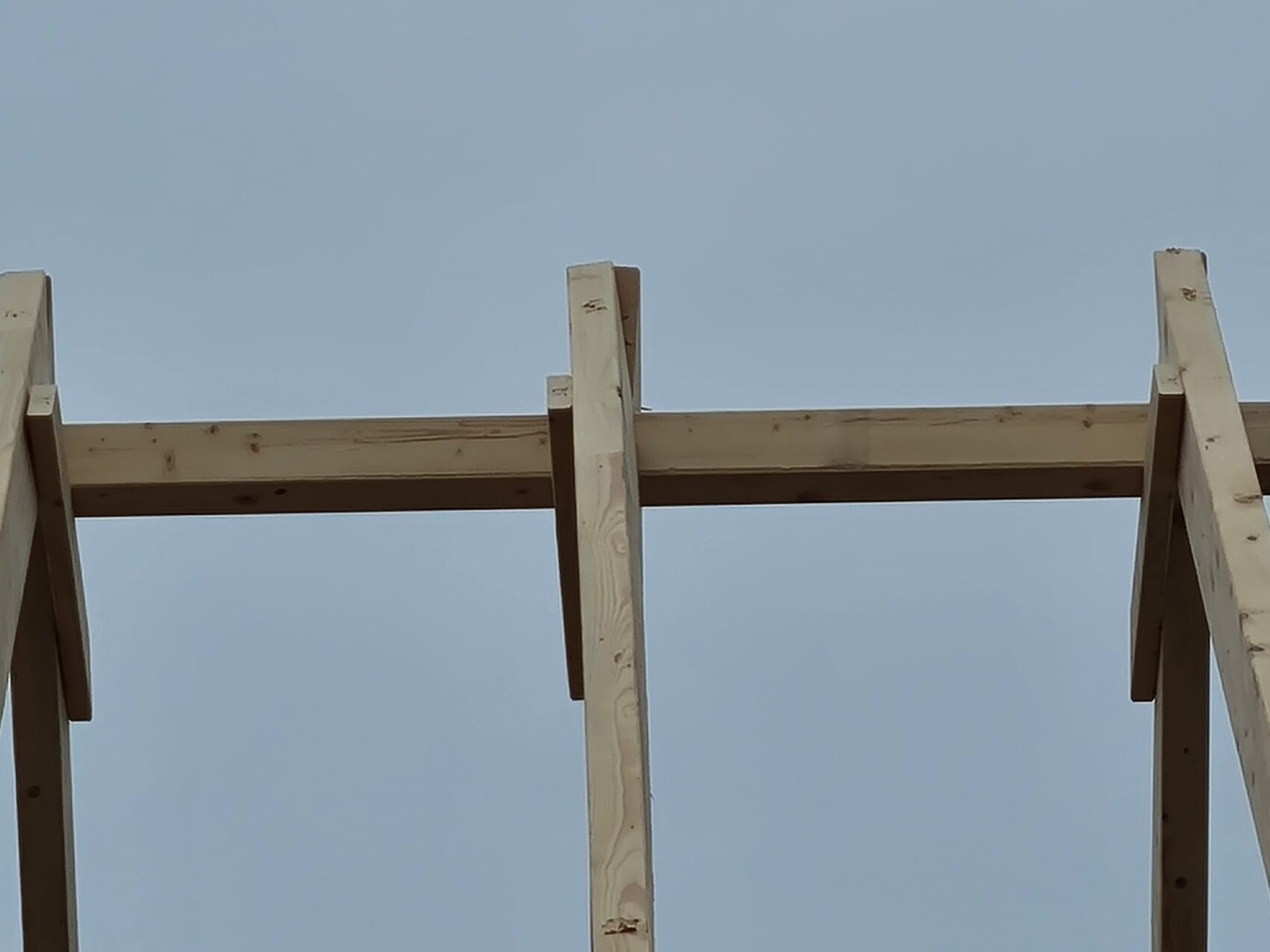 Holzgerüst aus Balken im Bau, sichtbar gegen blauen Himmel.