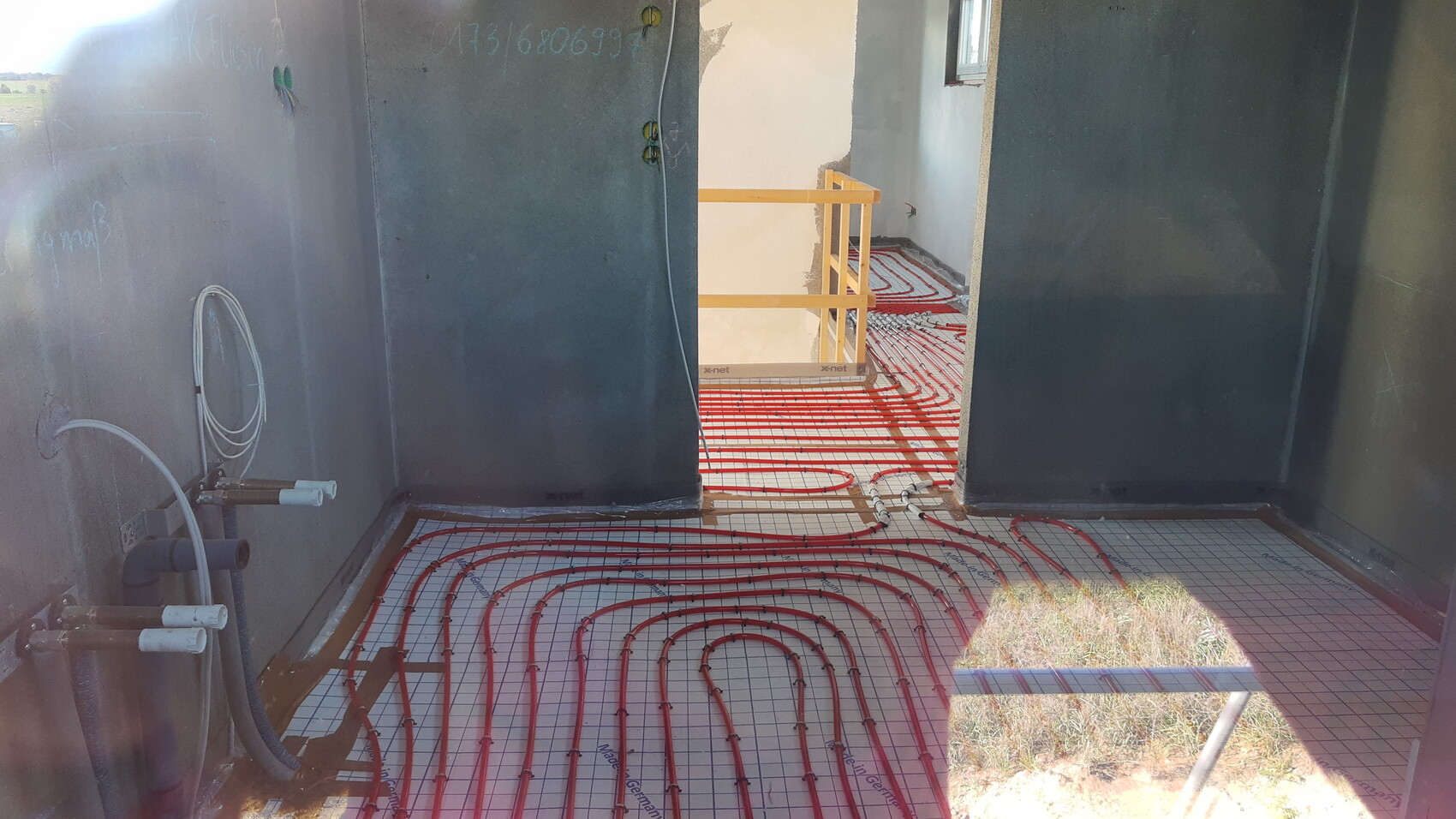 Underfloor heating: red pipes spiraled on mesh reinforcement on a construction site.