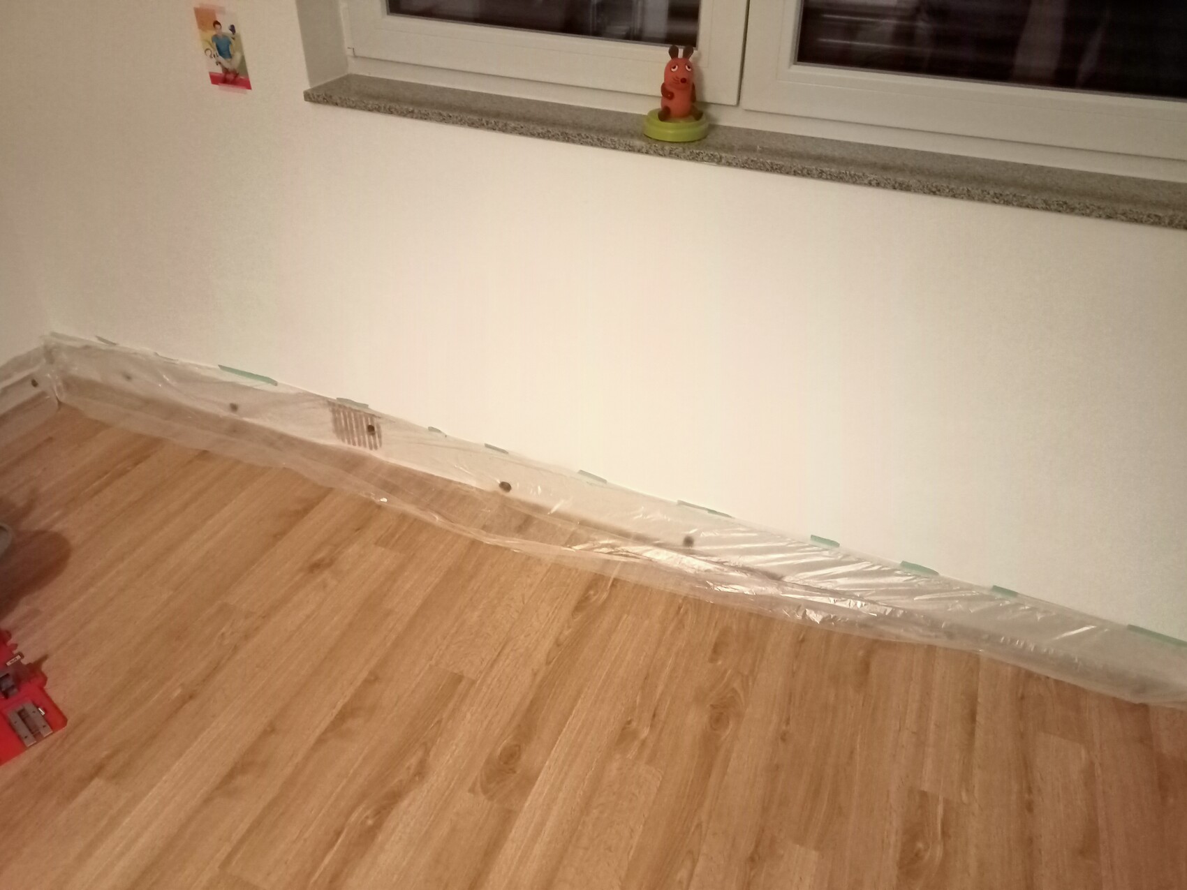 Ecke mit Holzboden; Folie schützt die Wandfußleiste, Fensterbank mit Spielzeugfigur.