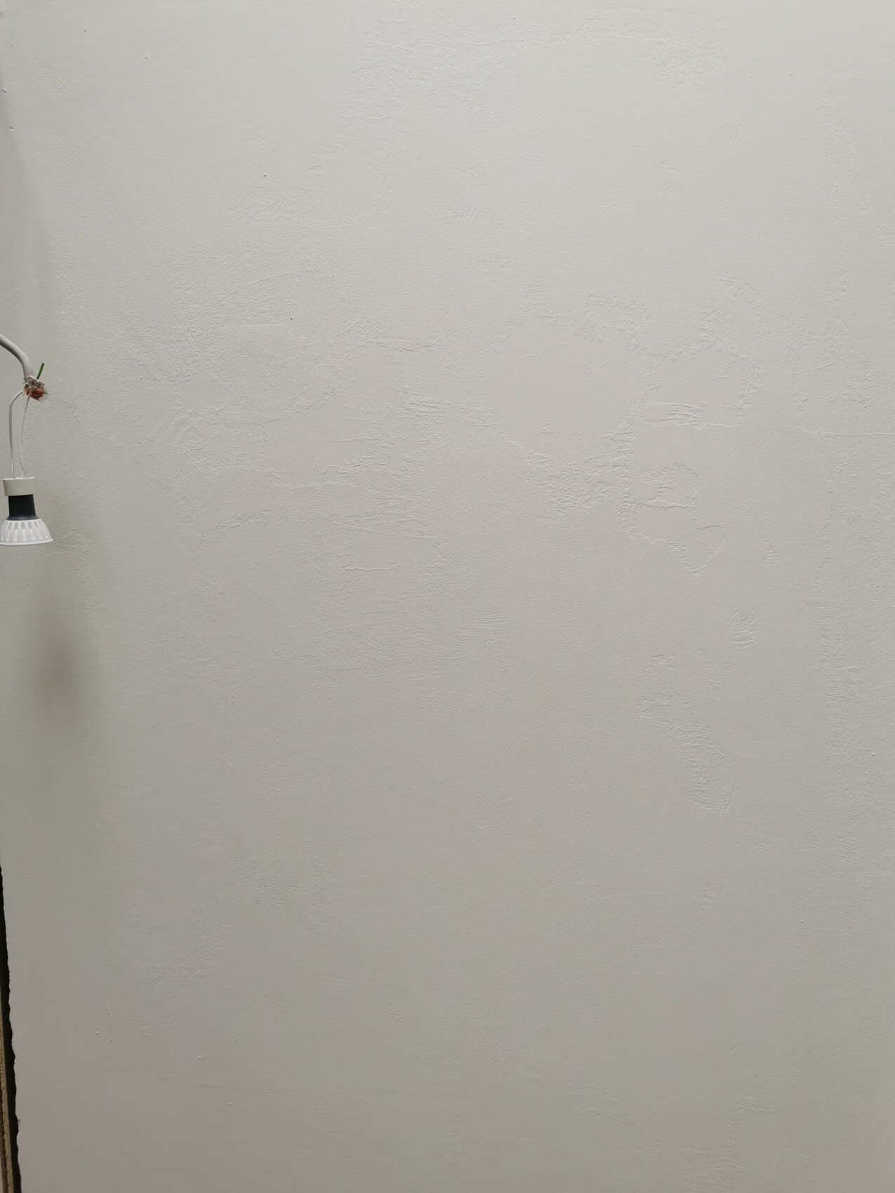 Plain textured white wall with a hanging lamp on the left and visible cables.