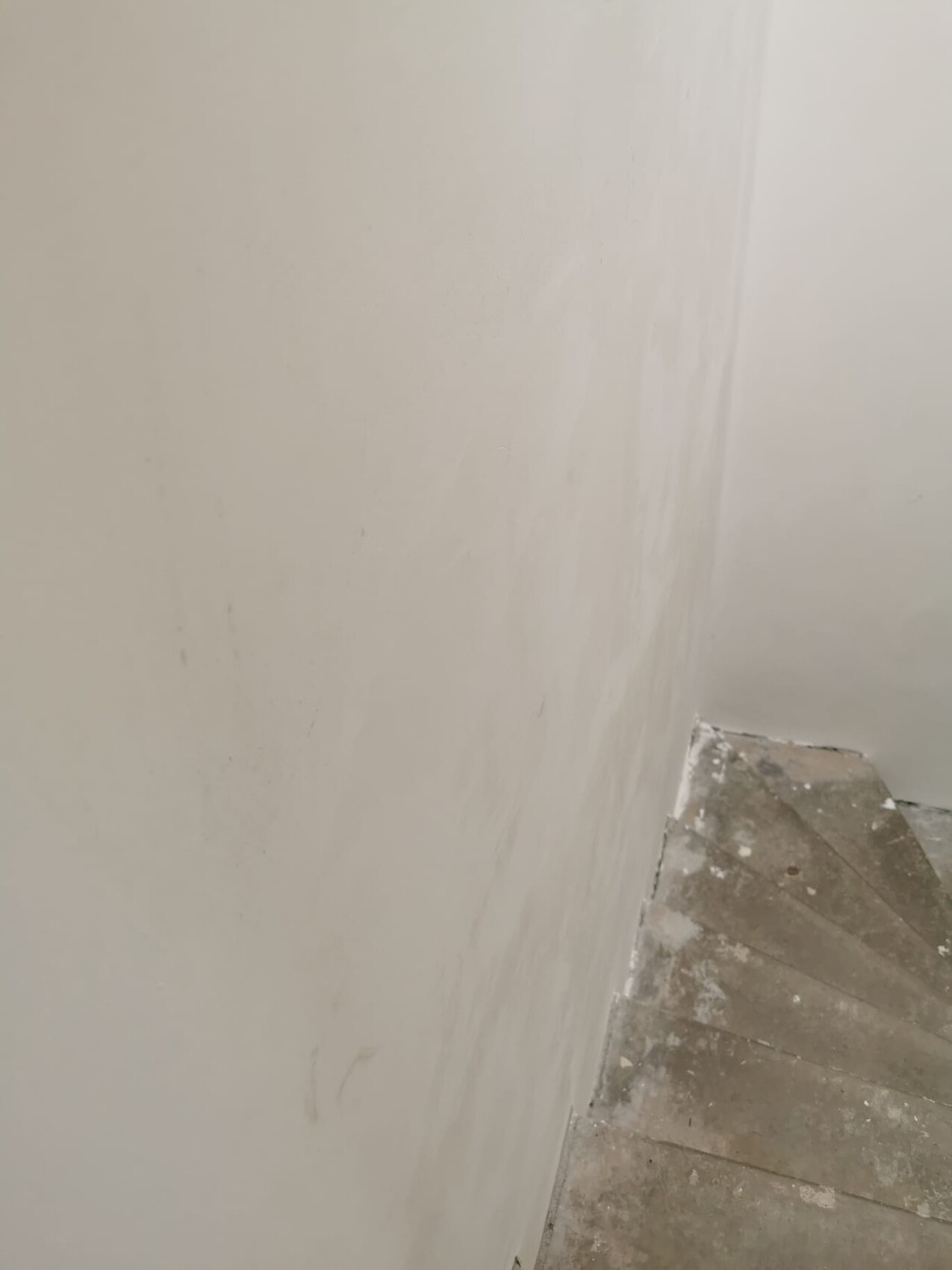 Corner of a staircase: white walls, dusty steps with plaster residue.