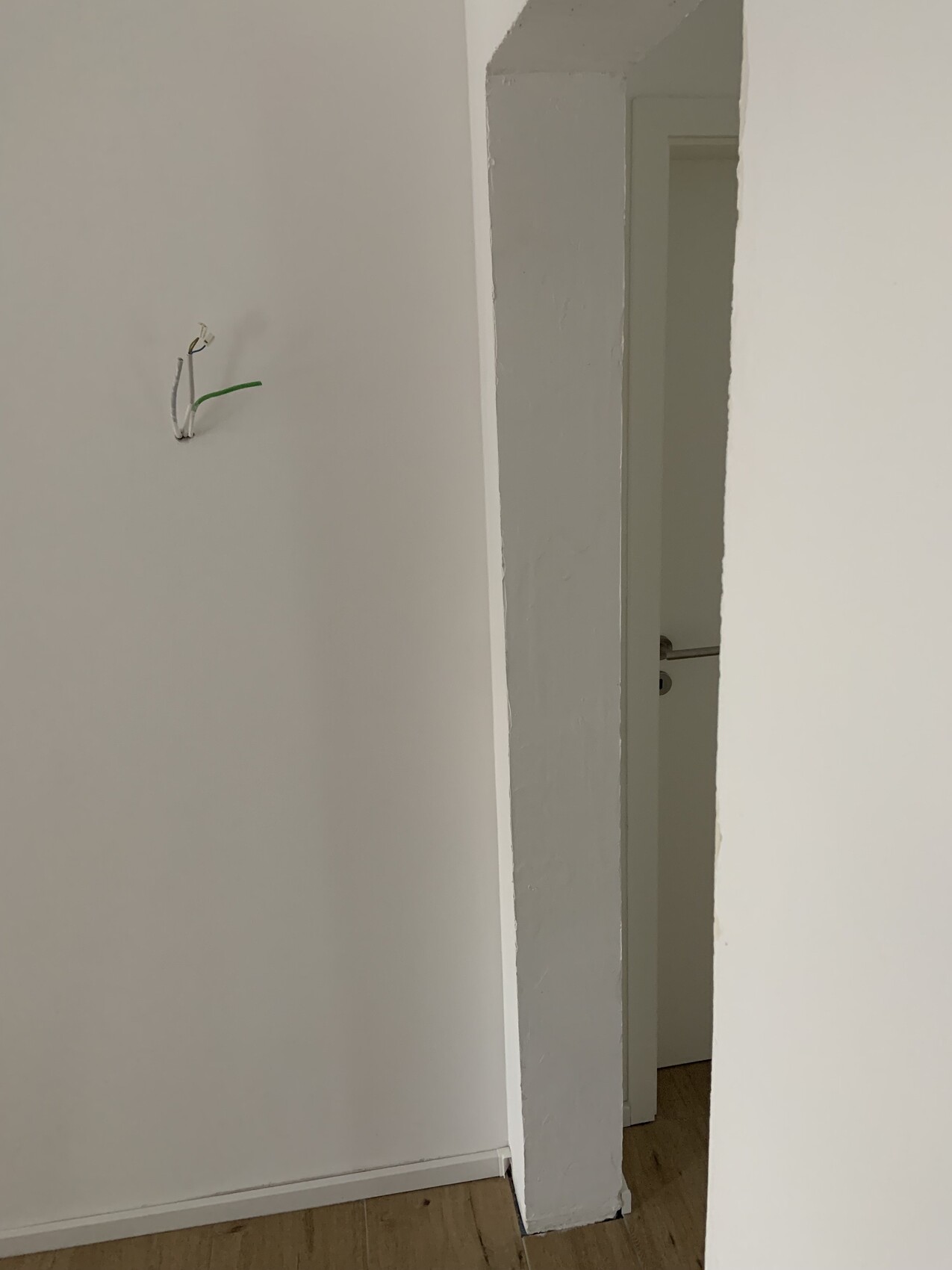 Exposed electrical wiring protruding from a white wall next to a door frame.