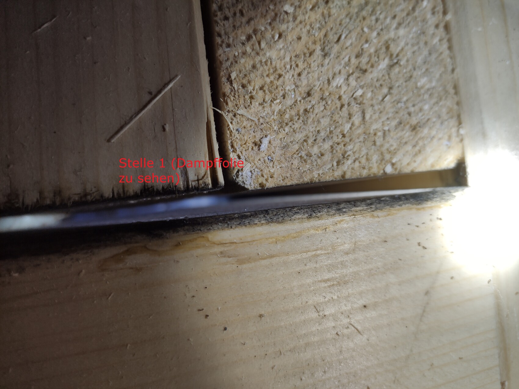 Nahaufnahme eines Holzrahmens mit sichtbarer Dampffolie in einer Fuge, unten Metallkante.
