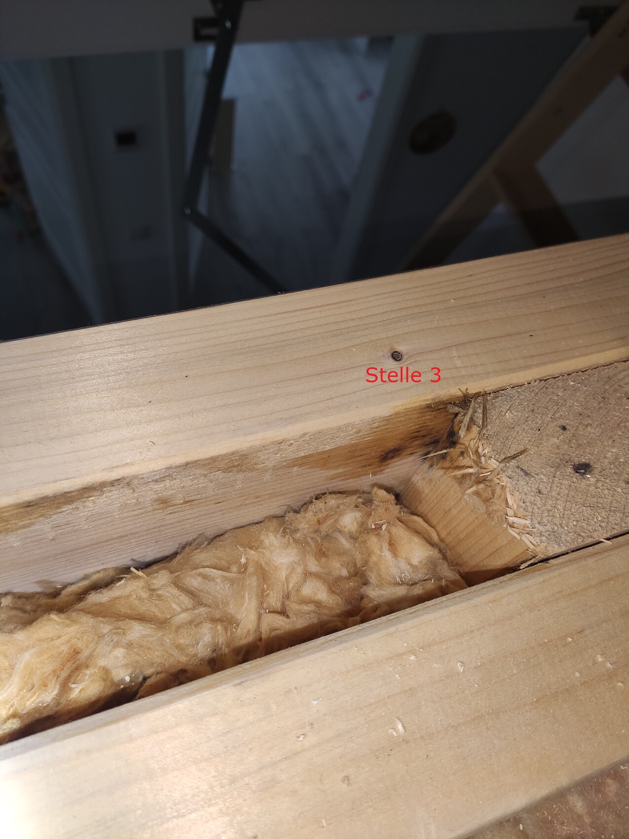 Holzbalken mit Dämmmaterial dazwischen; rote Aufschrift