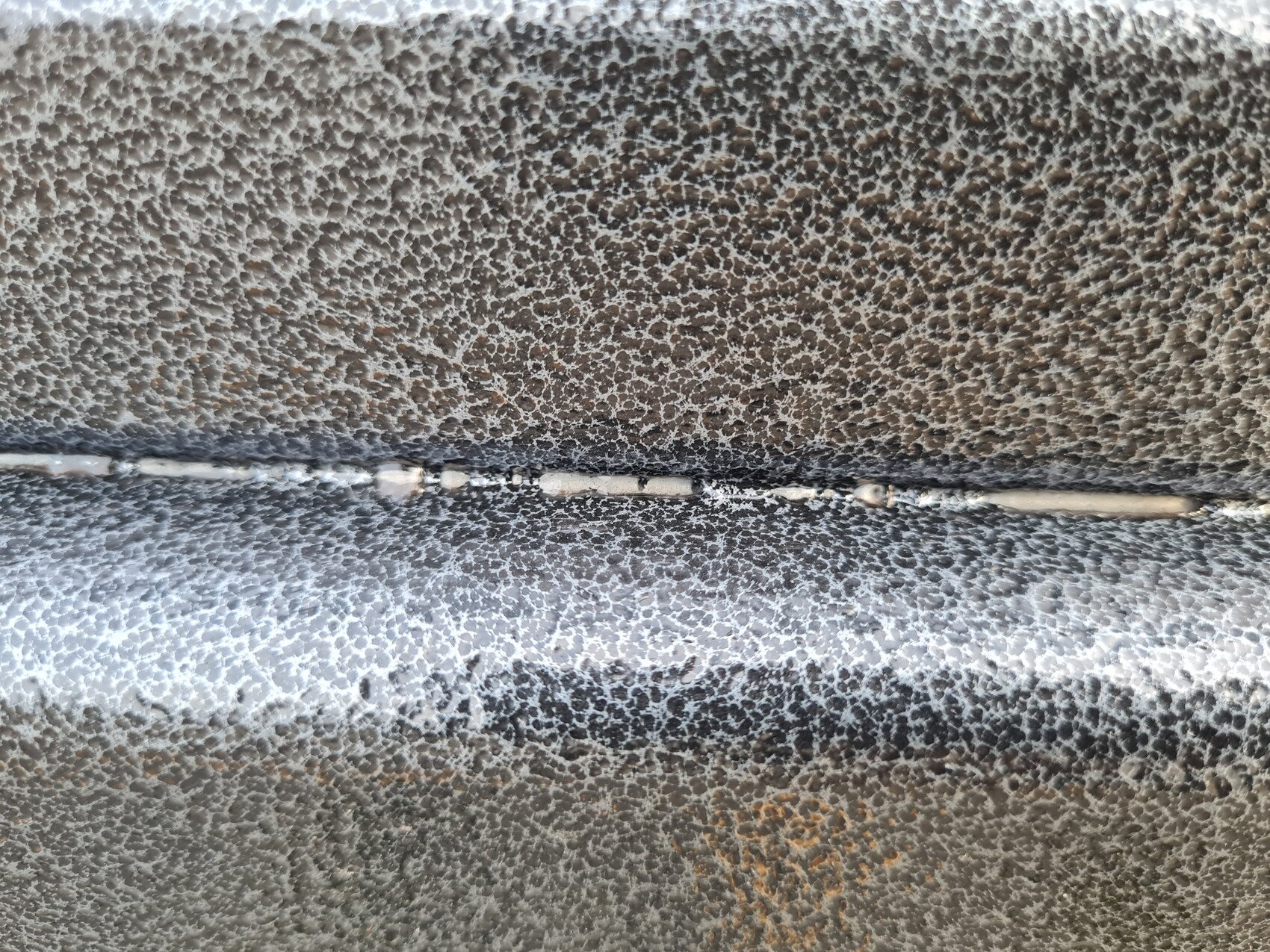 Close-up of a rough, embossed metal surface with a horizontal seam.