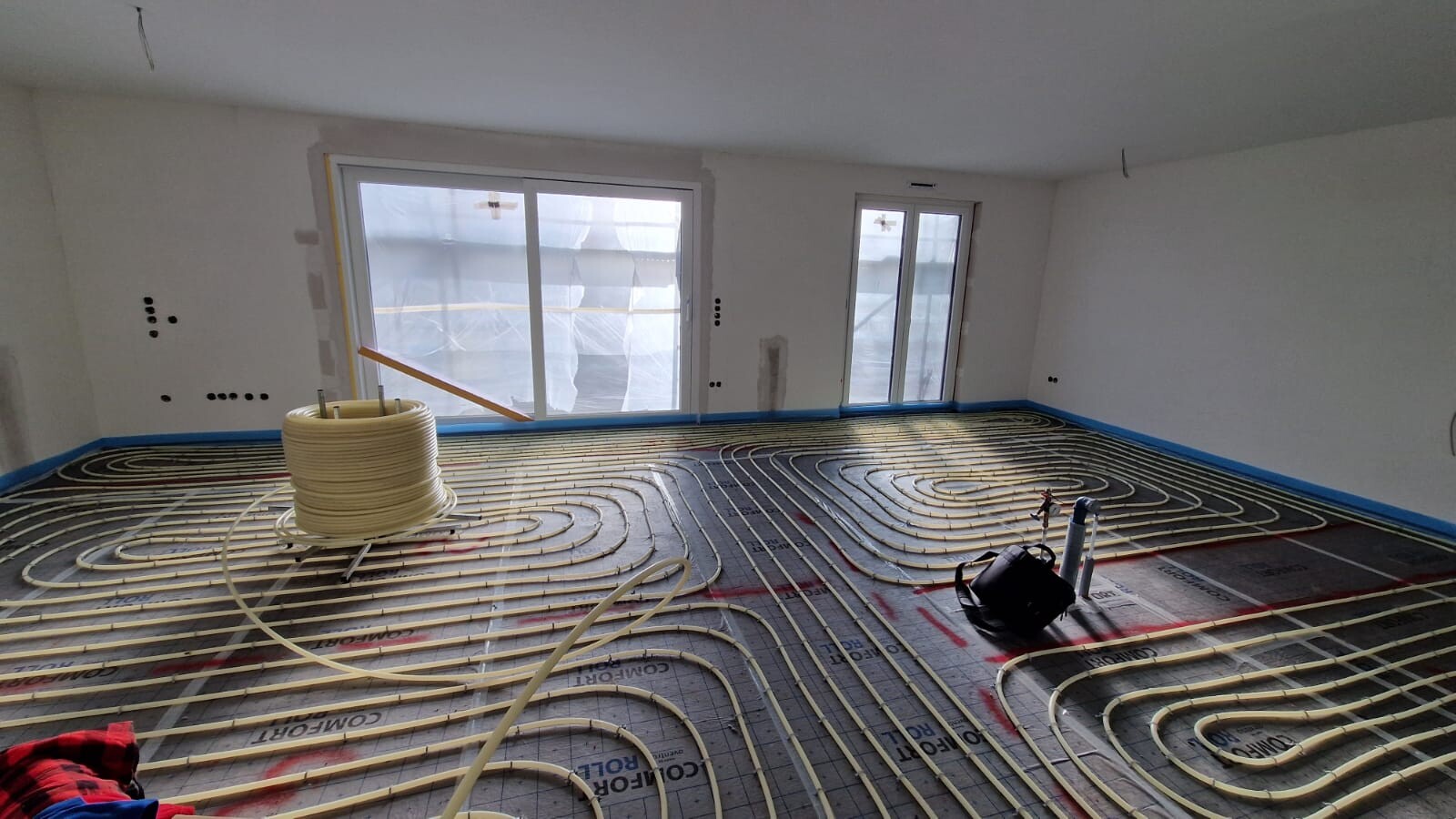 Fußbodenheizung wird installiert; Heizrohre spiralförmig auf dem Boden, Spule und Werkzeug.