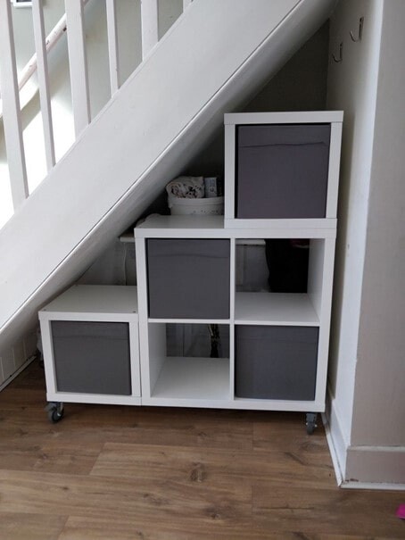 White modular storage unit with gray fabric boxes under the stairs on casters.