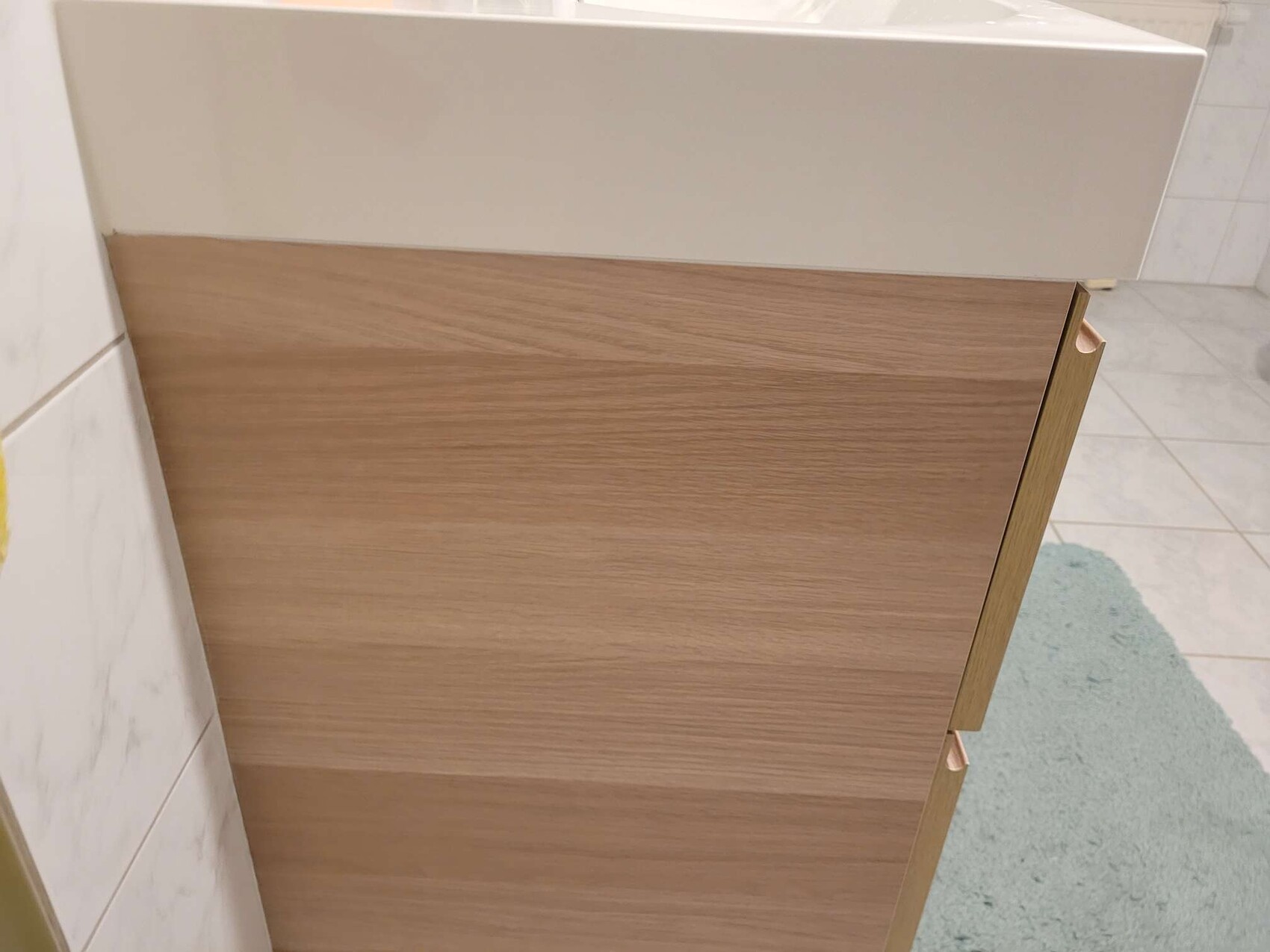 Modern bathroom base cabinet with wood finish and white washbasin top in bathroom.