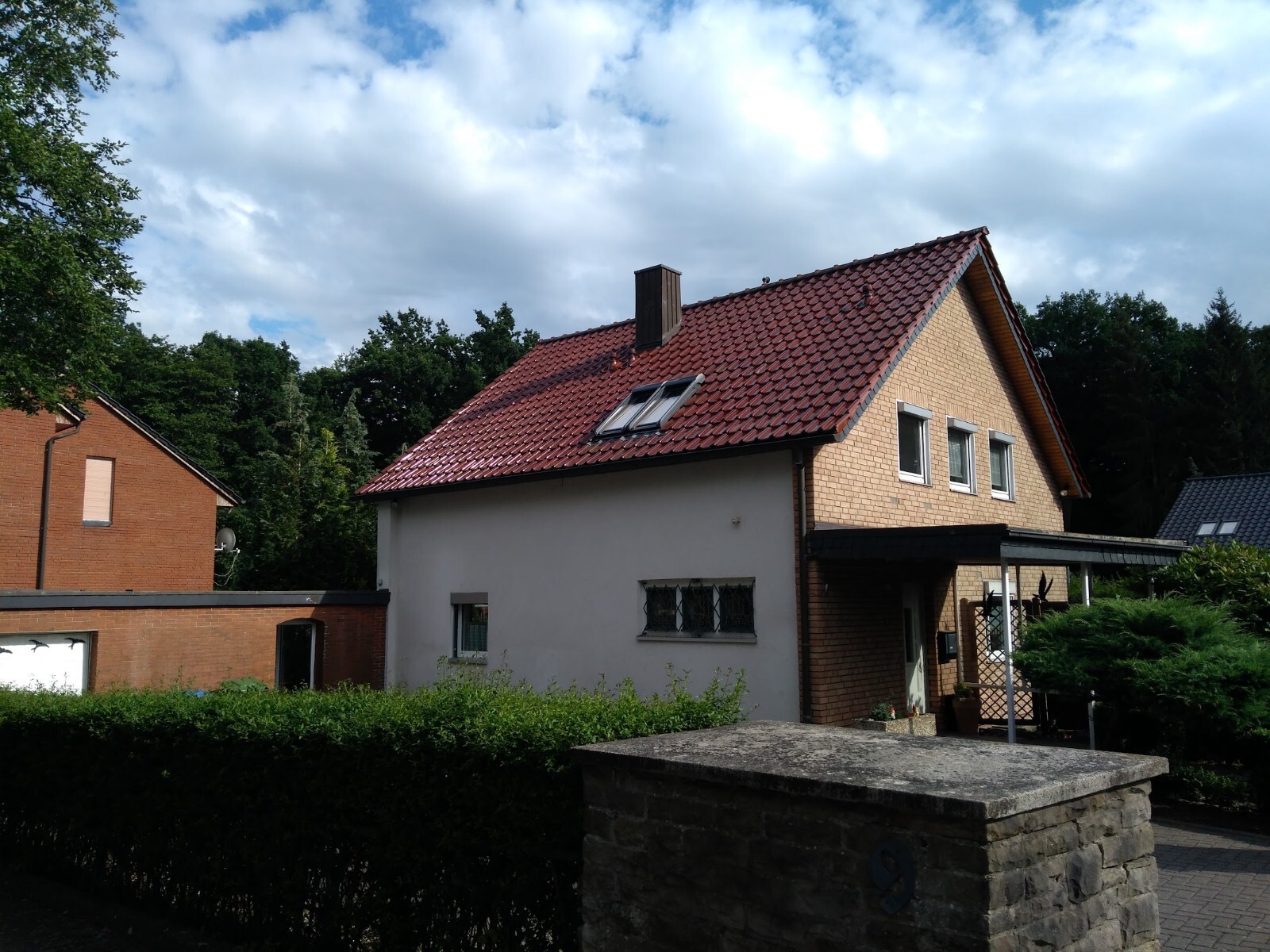 Two-story house with red tiled roof, roof windows, and hedge in the front garden.