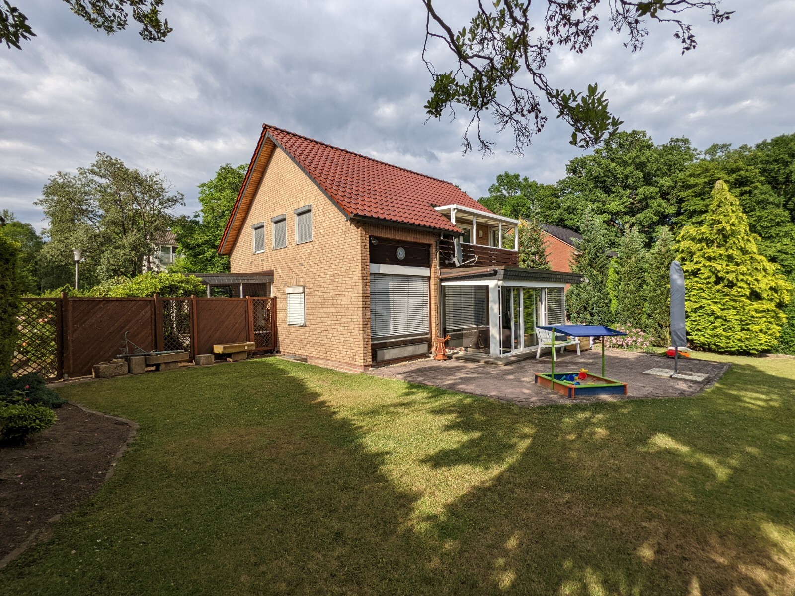 Two-story brick house with red tiled roof, glass veranda, garden with sandbox.