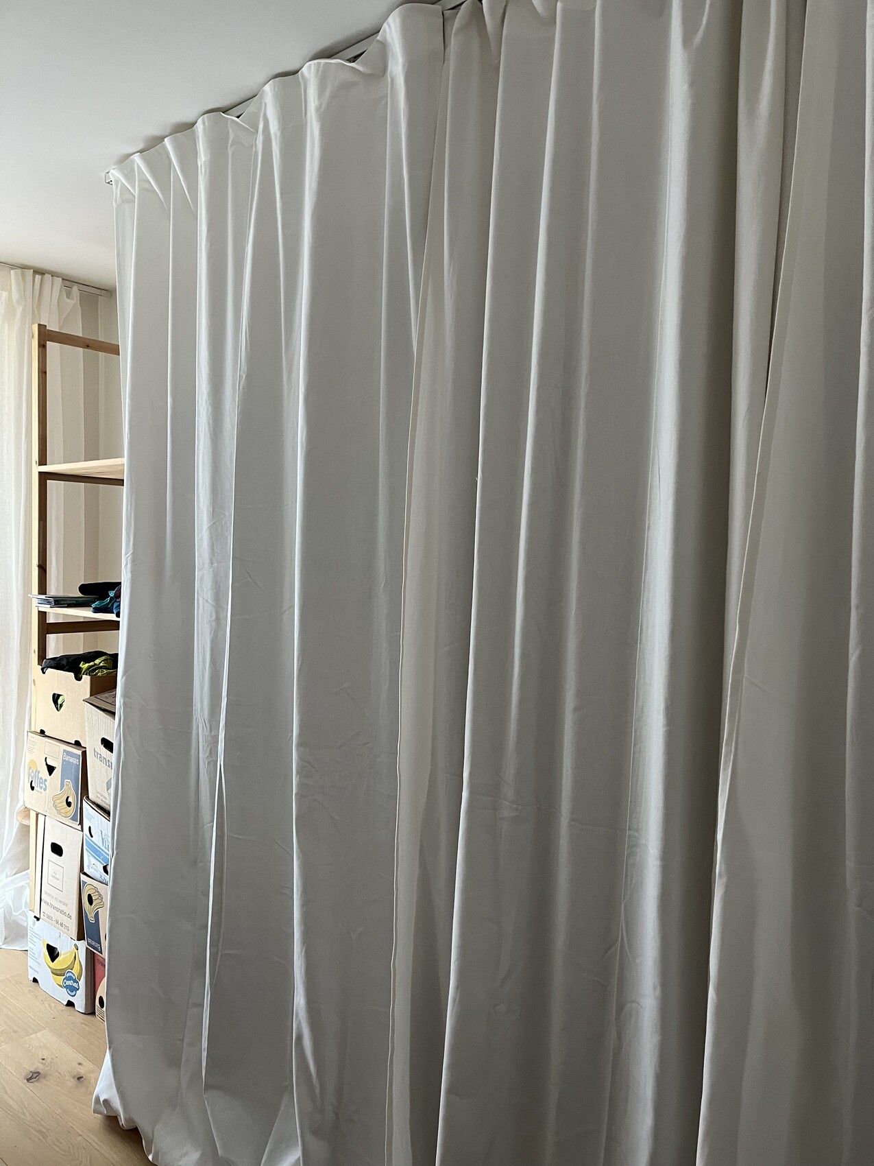 Large light gray curtains acting as room dividers; behind the curtain a wooden shelf with boxes.
