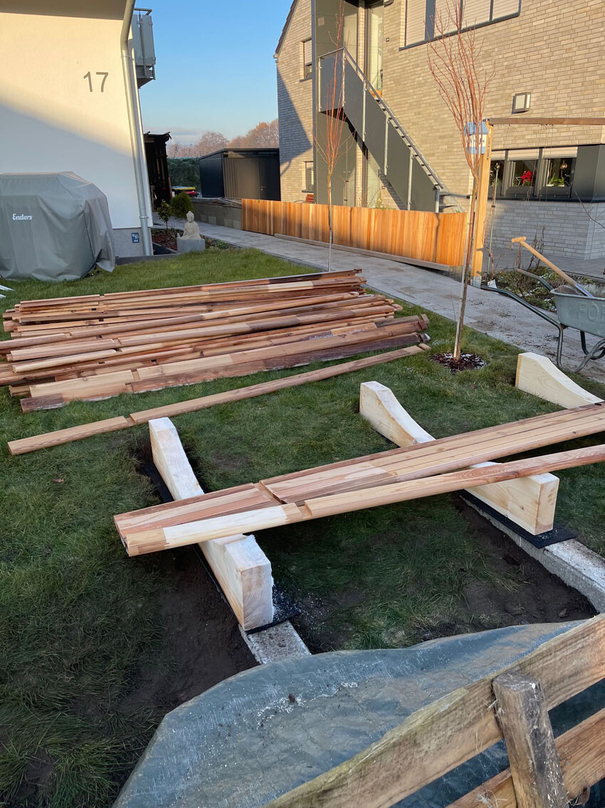 Construction site in the courtyard: stacked wooden planks, temporary bridge over ditch, wheelbarrow on the right.
