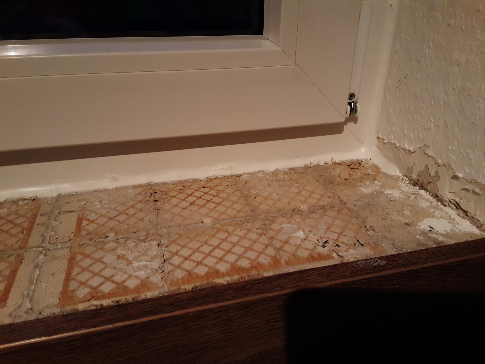 Fensterbank mit beschädigtem Putz, bröckelnde Wand und alte Bodenfliesen