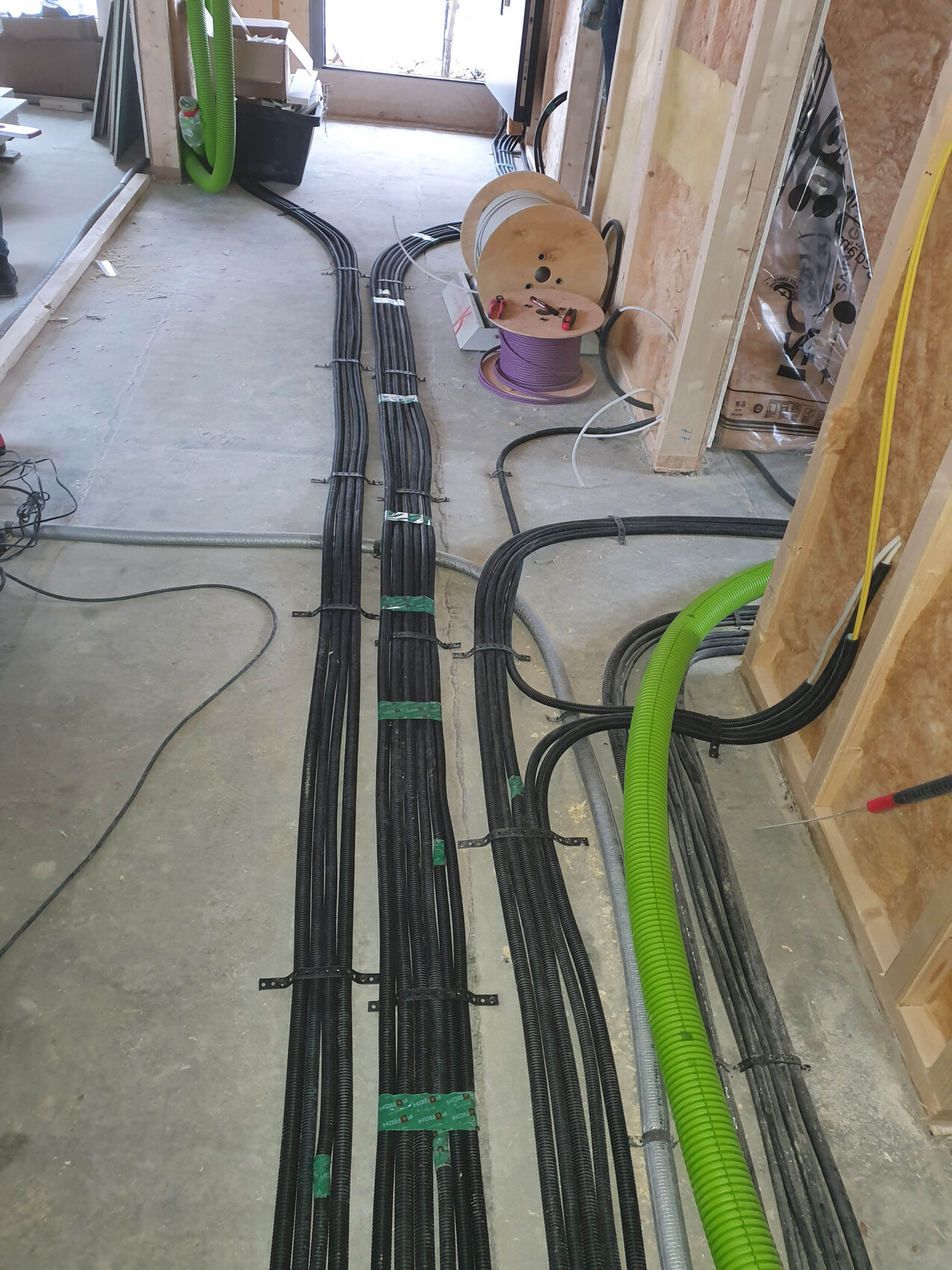 Construction site: Several black cable bundles and green pipes lying on the floor, spool with cable.