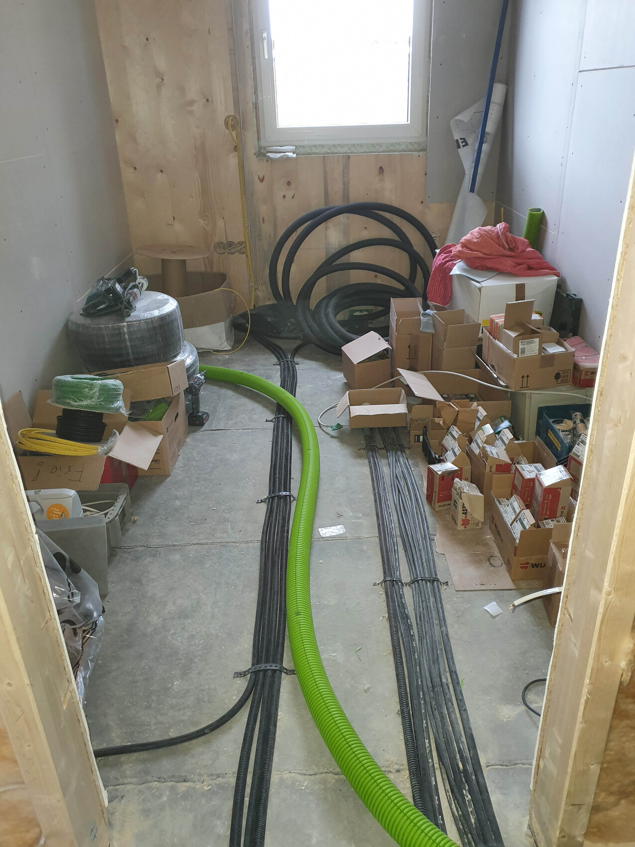 Construction room with black cable bundles, green hose, and boxes.