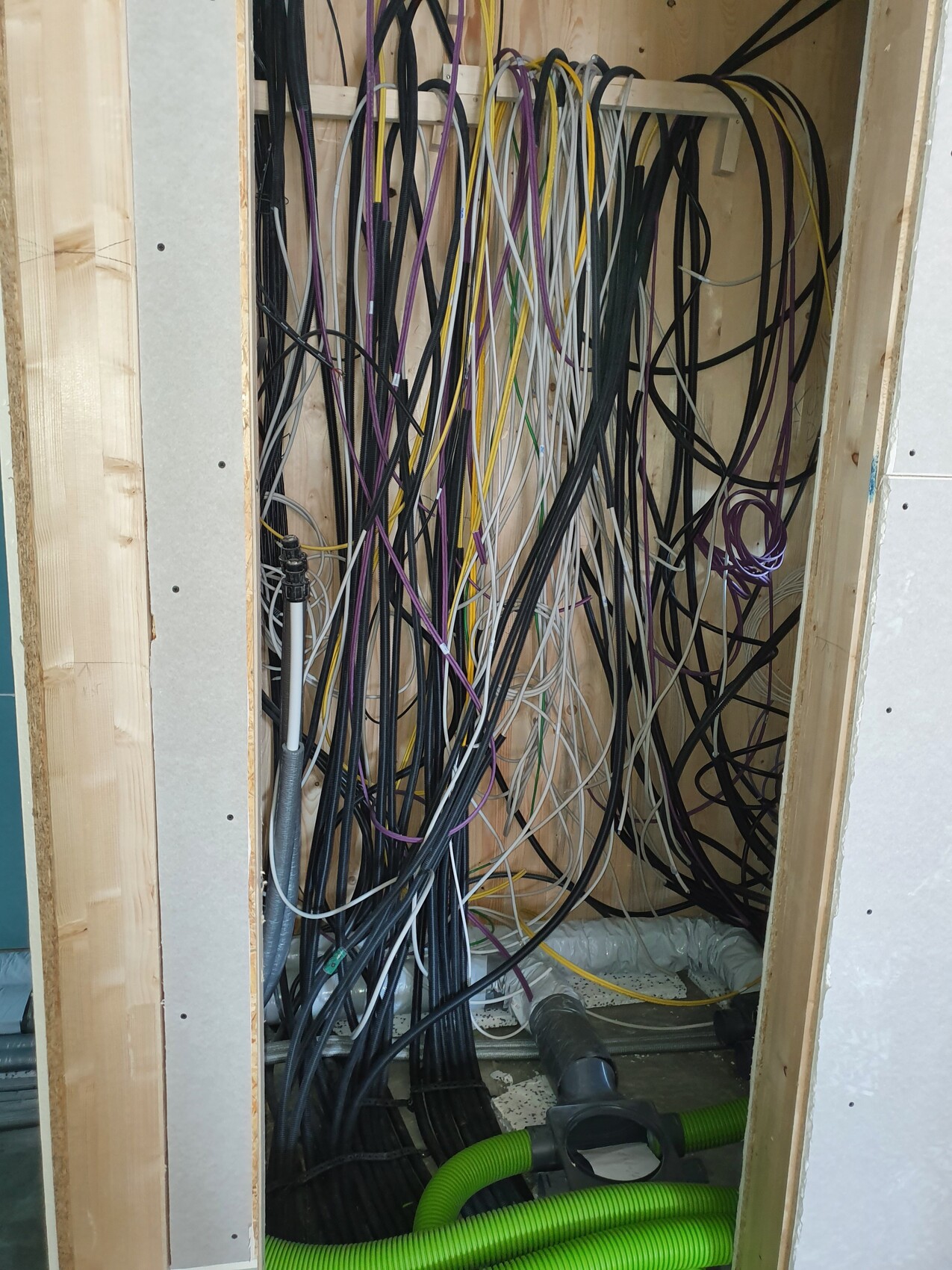 Cable chaos: colorful wires hanging in a wall niche, green hoses at the bottom.