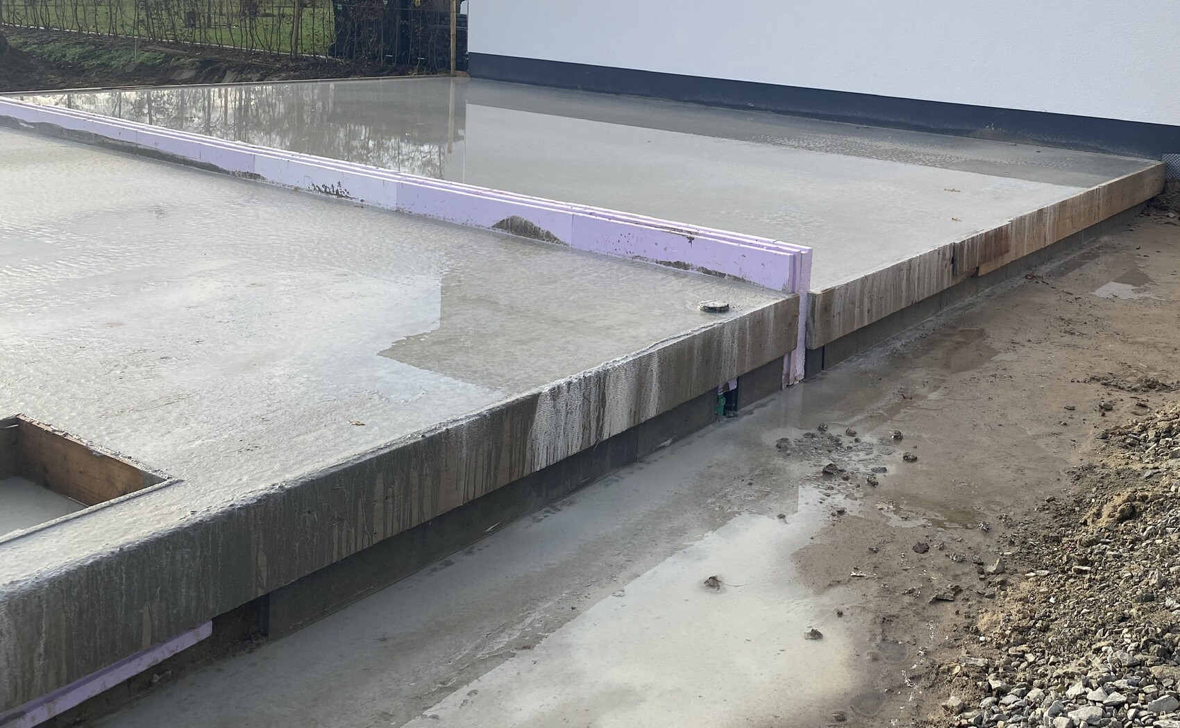 Frisch gegossene Betonplatte mit lilafarbenem Styropor-Rand, schlammigem Untergrund.