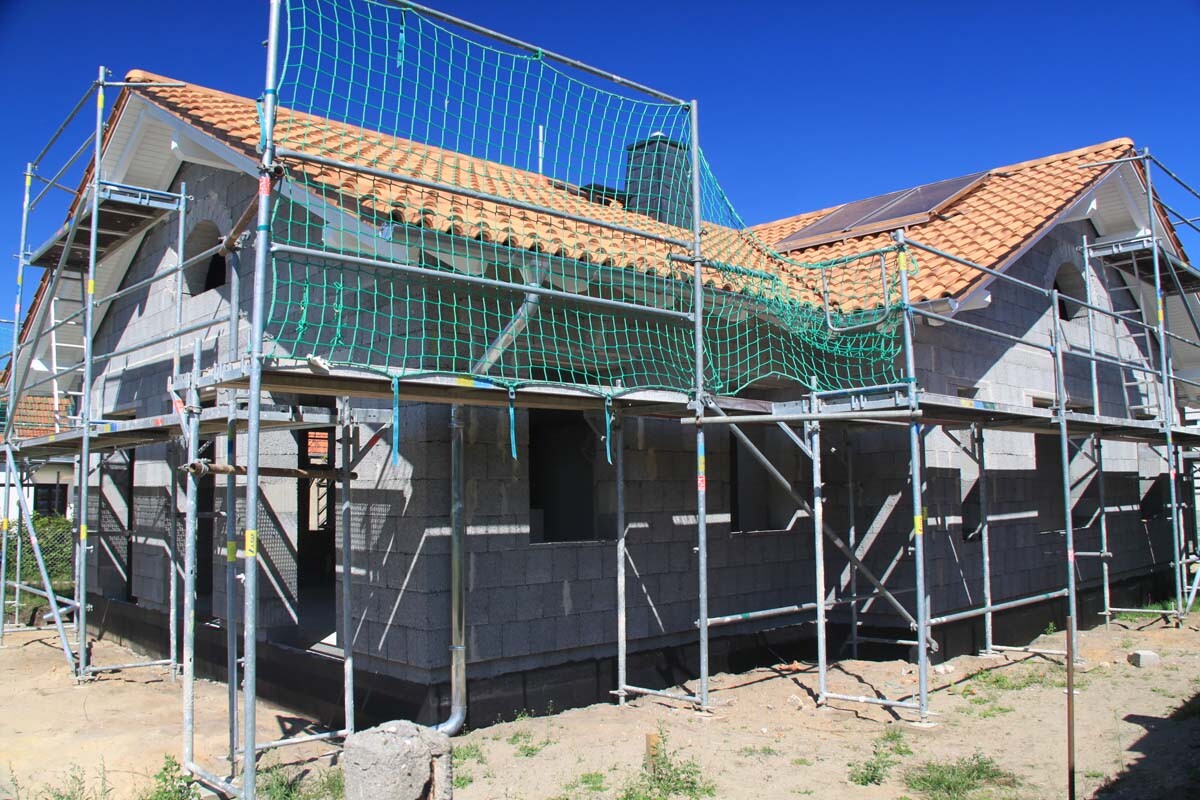 Rohbau eines Hauses mit Gerüst, grünem Schutznetz und Ziegeldach.