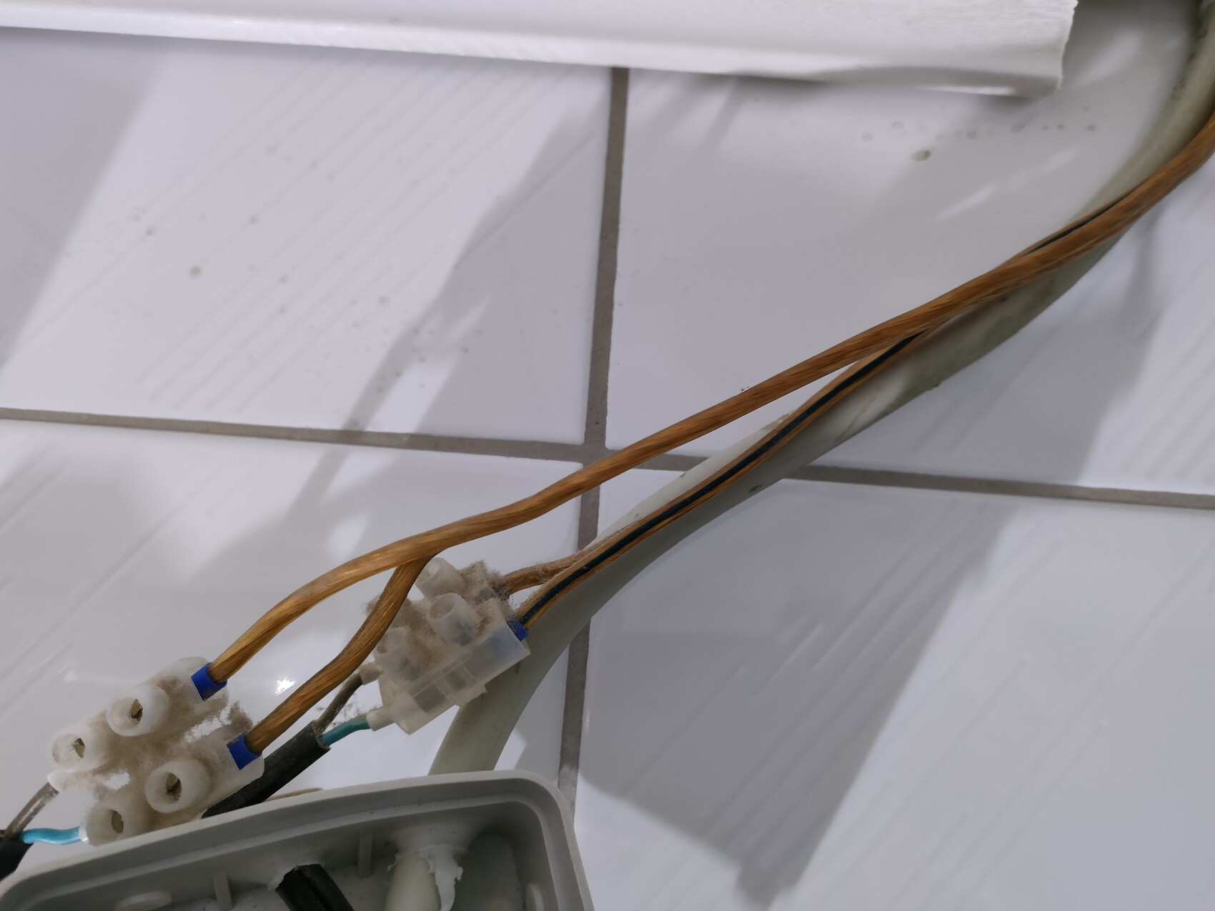 Nahaufnahme von braunen Kabeln mit Steckern auf weißen Fliesen; Elektroinstallation.