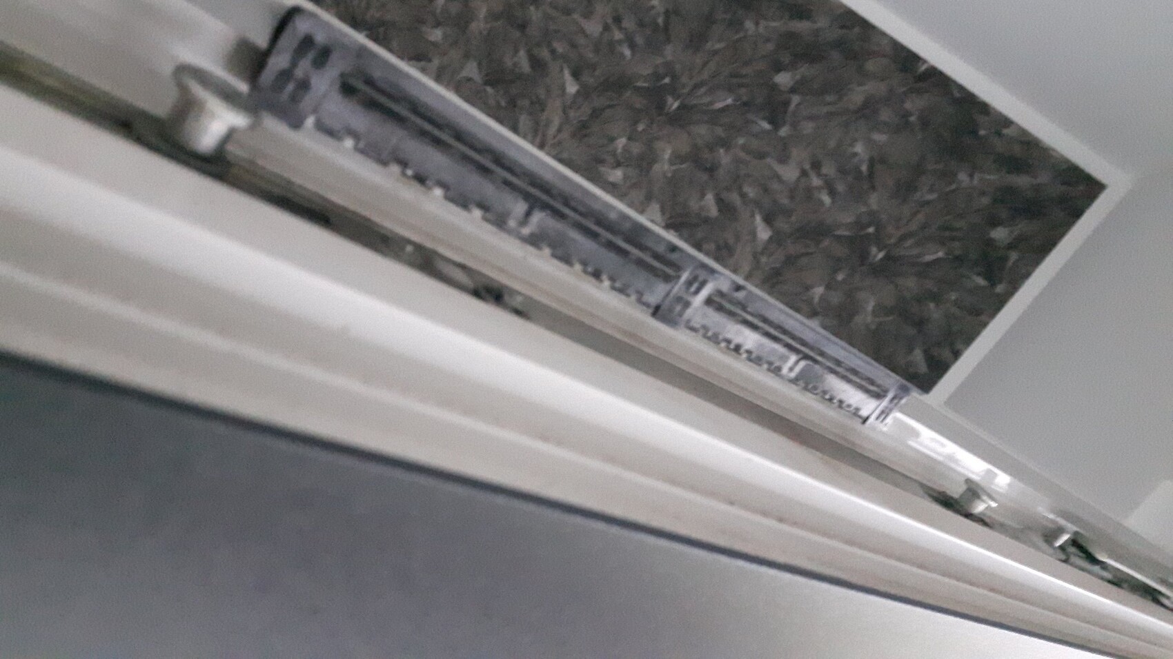 Close-up of a metal drawer slide on a white furniture edge, dark tiled background.