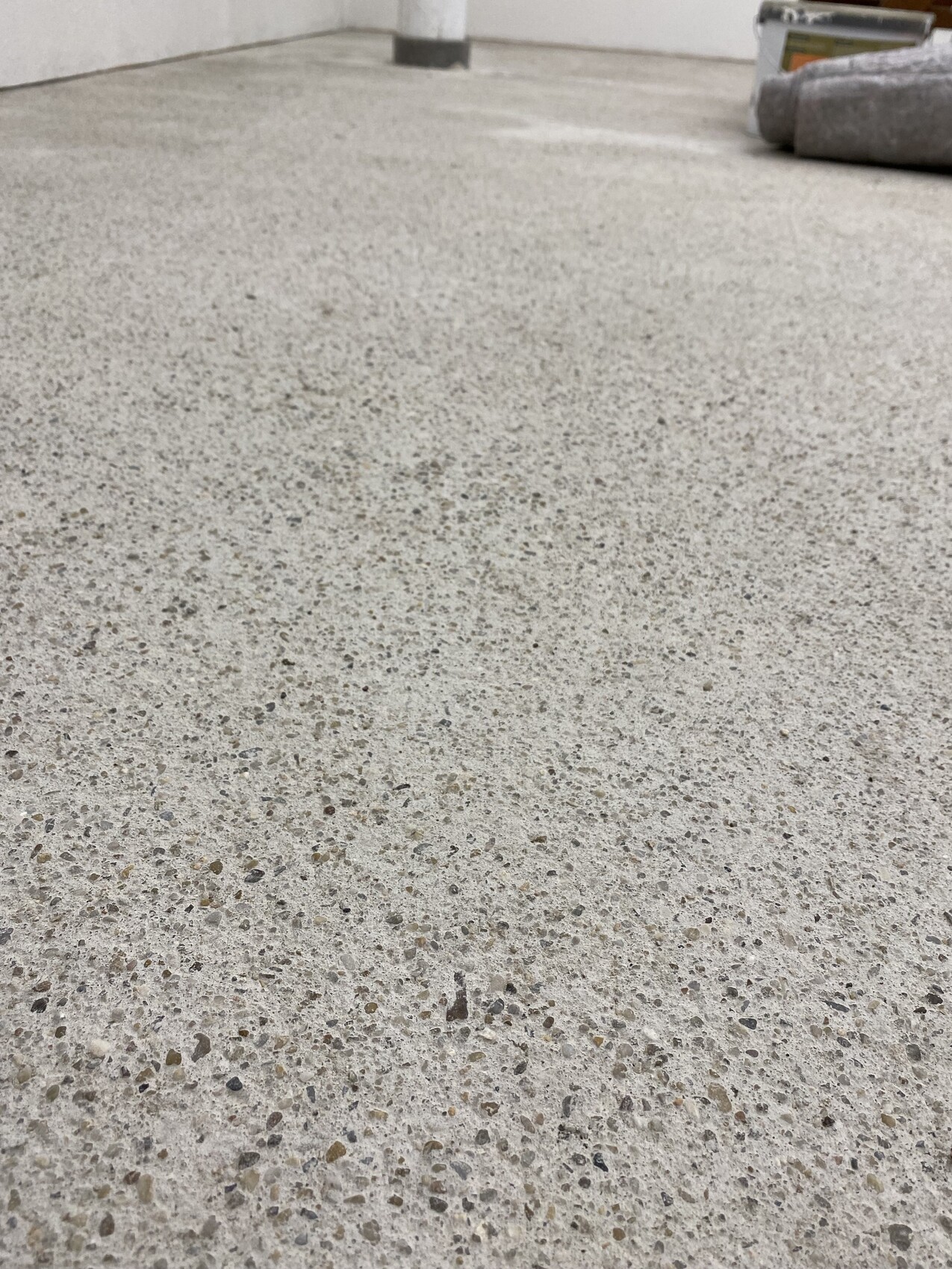 Coarse patterned concrete/terrazzo floor indoors; paint can and paint roller are in the upper right.