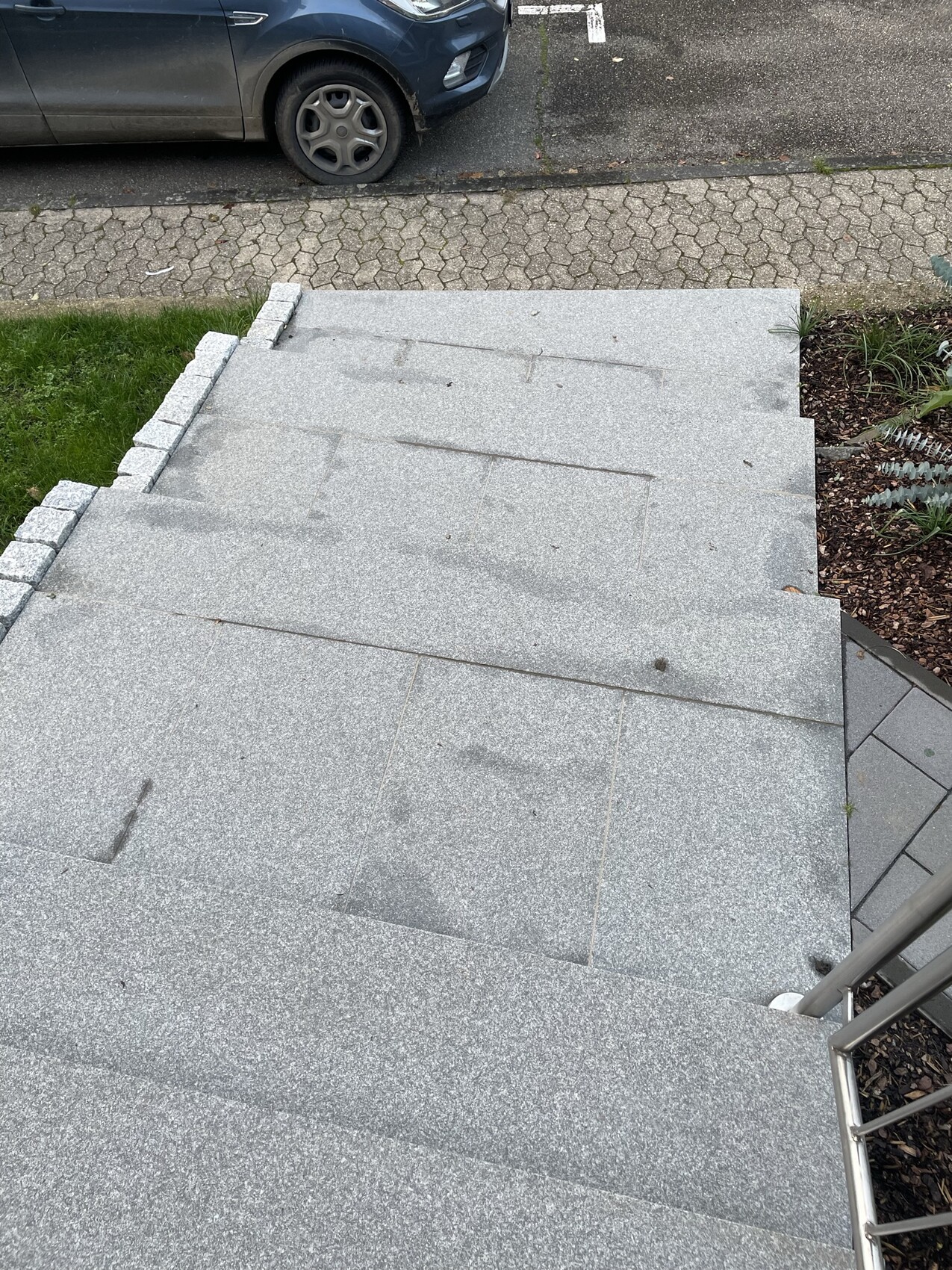 Gray stone stairs with railing leading down; street and parked car in the background.