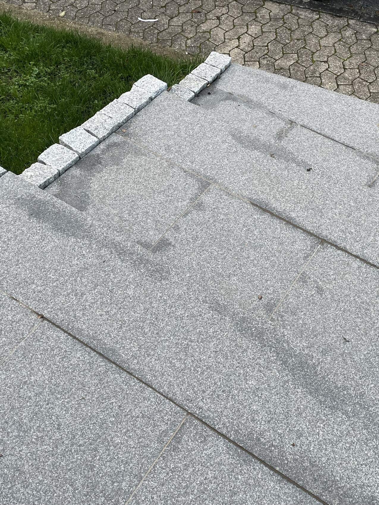 Top view: gray roof surface with small stone edging, grass on the left, paved path behind