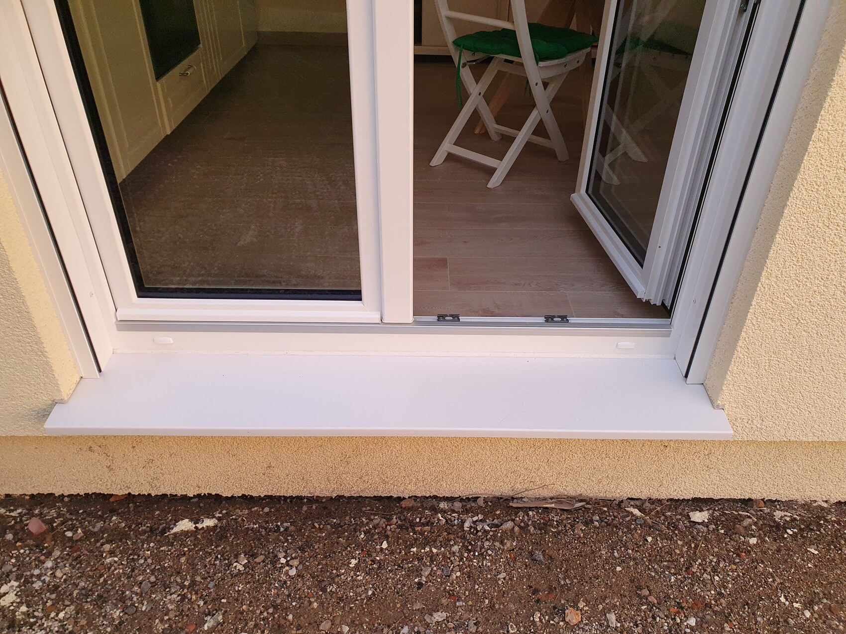 White glass sliding door opens into living room, interior with wooden floor and garden chair