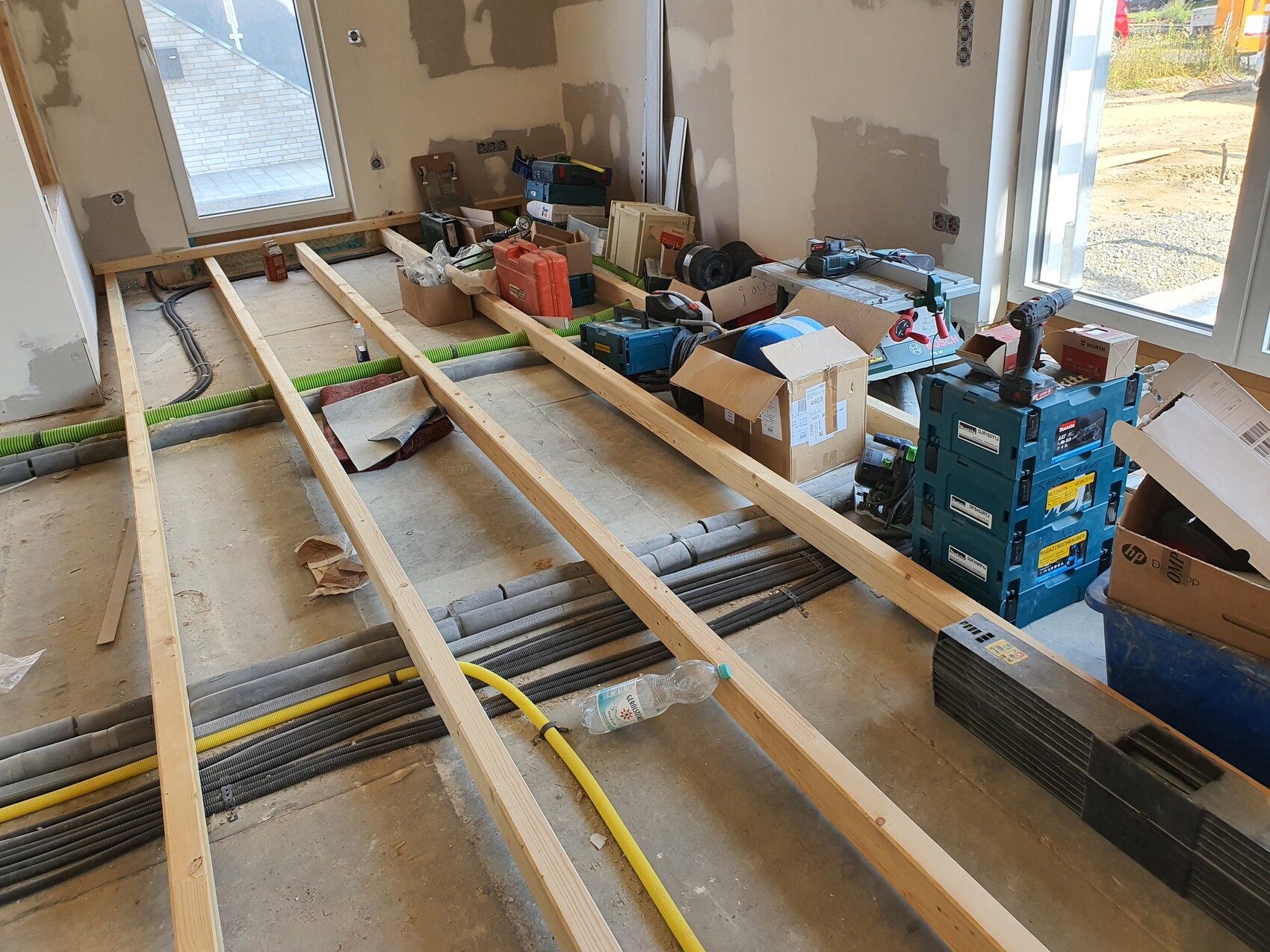 Rohbaustelle: freigelegte Bodenbalken, Werkzeuge, Kartons und Leitungen im Zimmer.