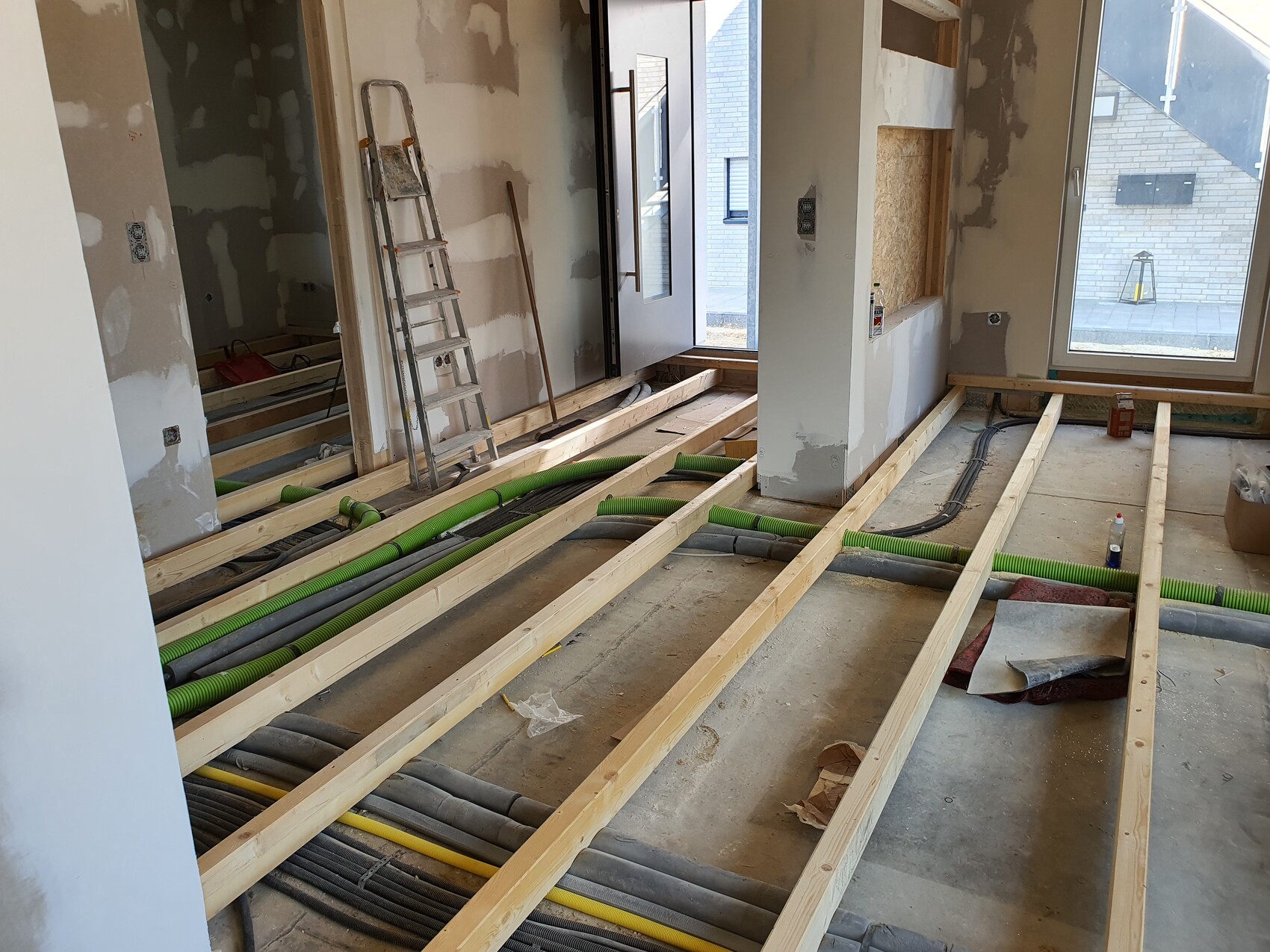 Renovierungsbaustelle: Holzbohlenboden, grüne Rohre, Leiter, unfertige Wände, Fenster