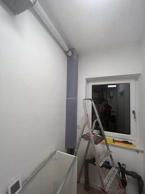 Renovation room: Ladder in front of window, pipes on ceiling, tools on table.