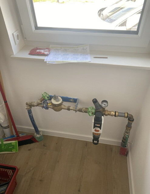 Water installation with pipes, shut-off valves, water meter, manometer and filter near window.
